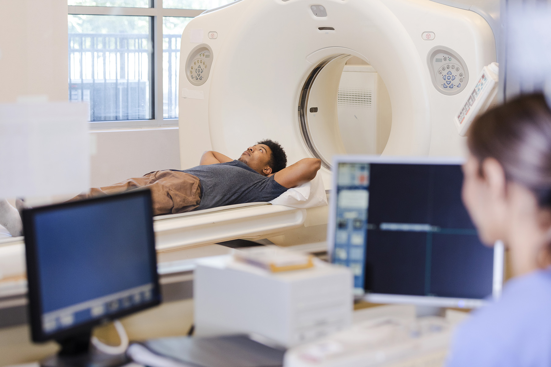 A man lies out stretched on the patient bed as the technician starts the CT scan.

