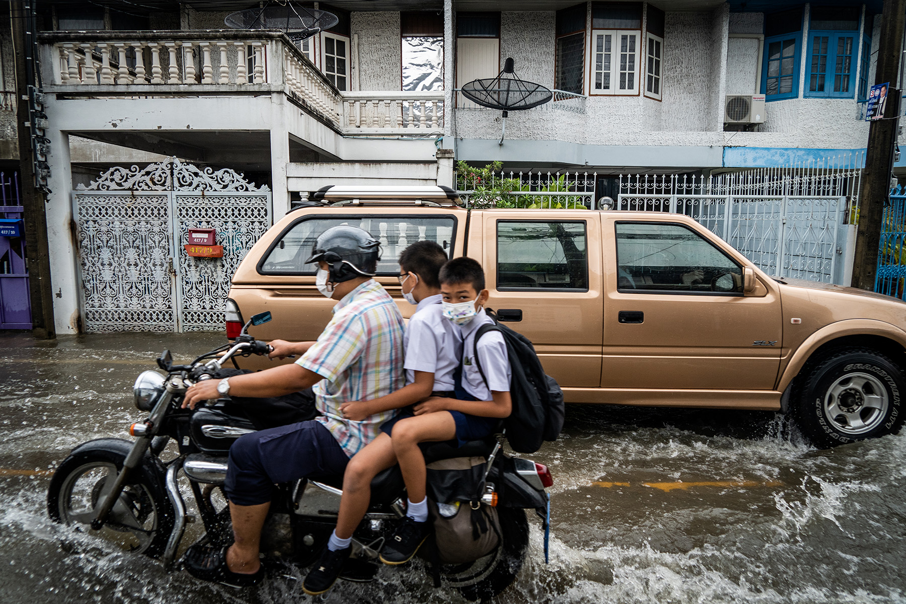 Teenage boys commute to school on a motorcycle during heavy flooding in Bangkok.

