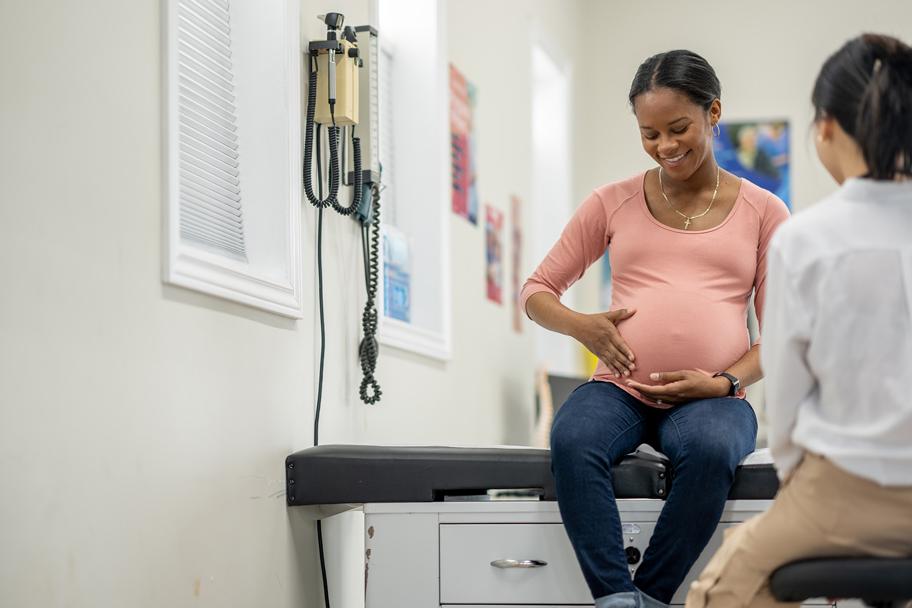 A pregnant woman smiles, as she sit up on an exam table in her doctors office during a routine prenatal check-up.