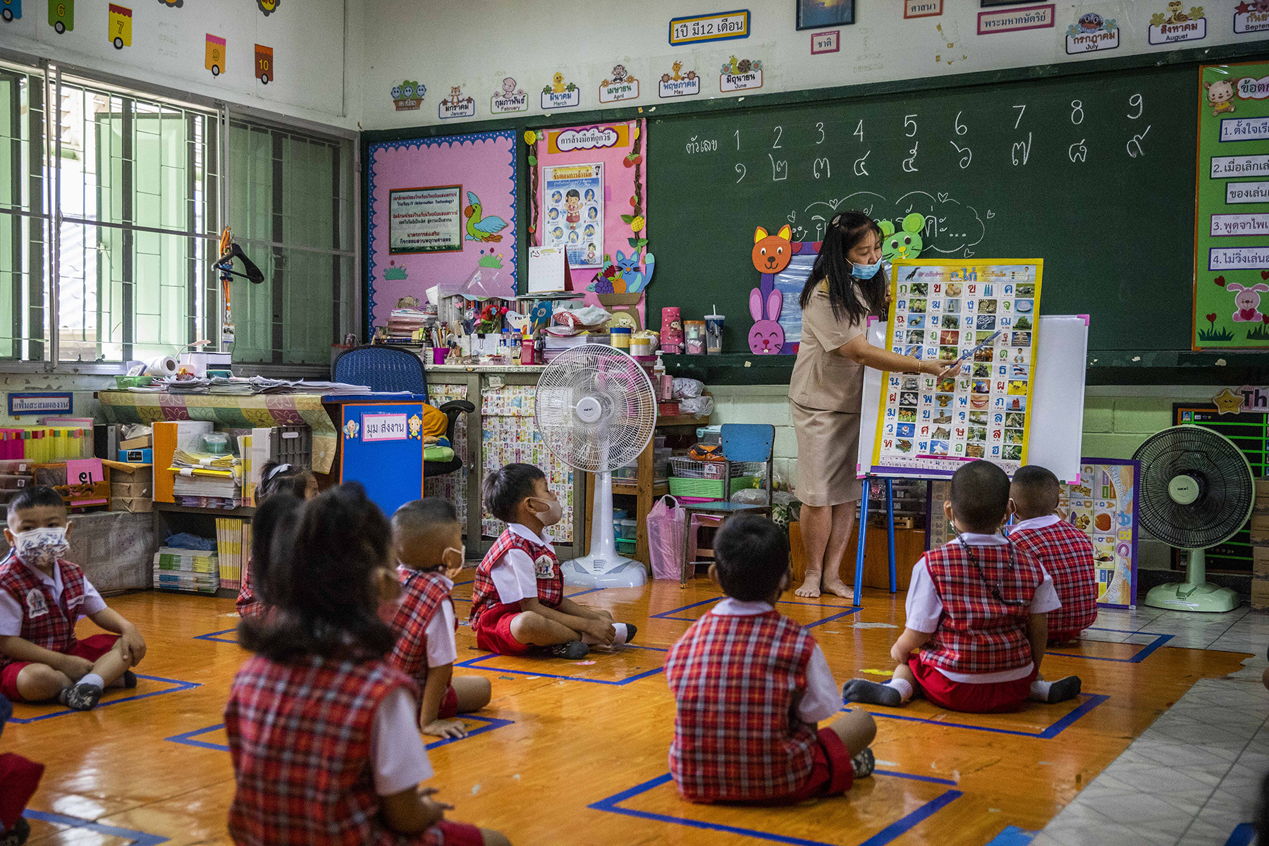 kindergarten pupils sit on the floor on their mats and listen to the teacher giving a lesson