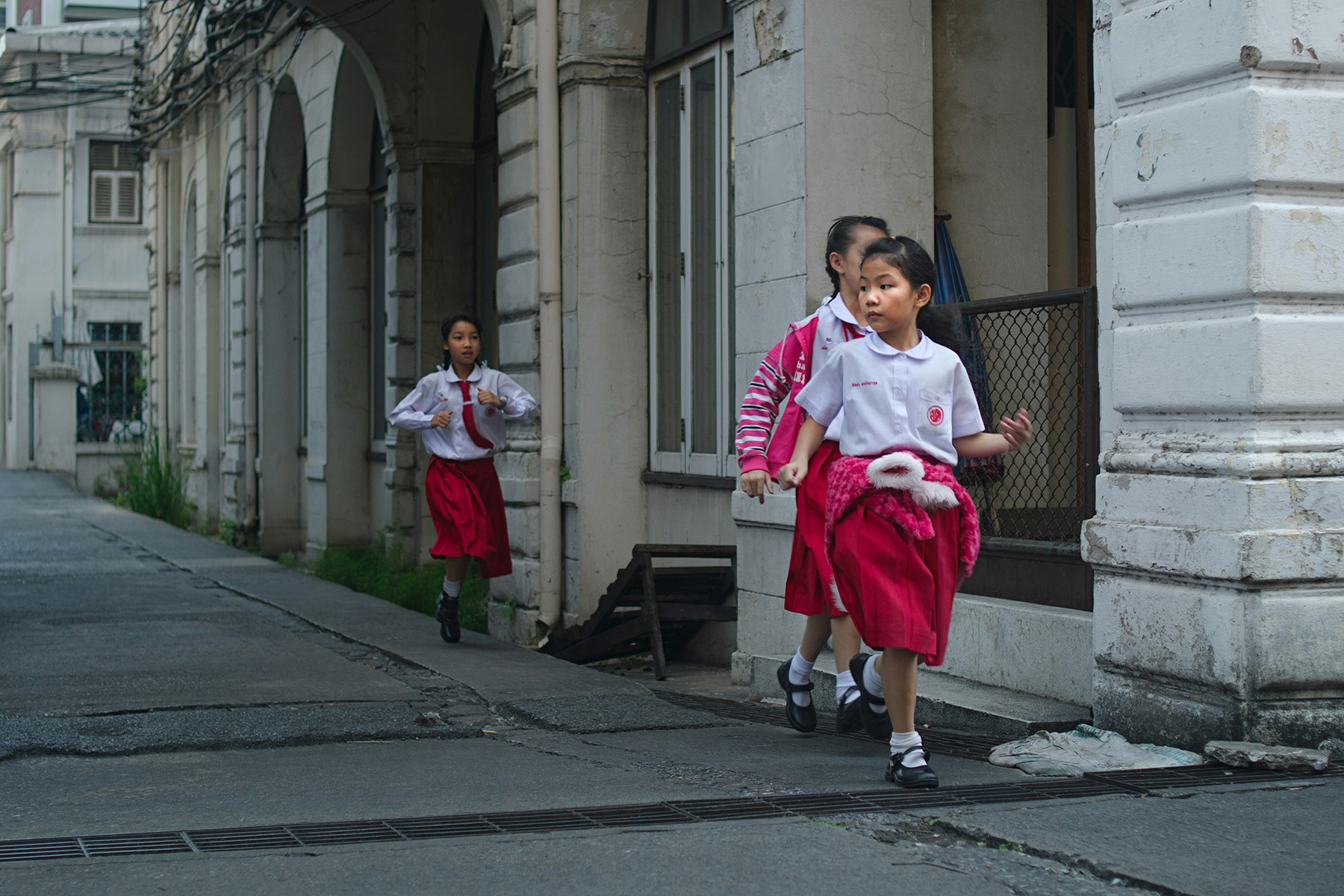Three girls in school uniforms running on the way to school.

