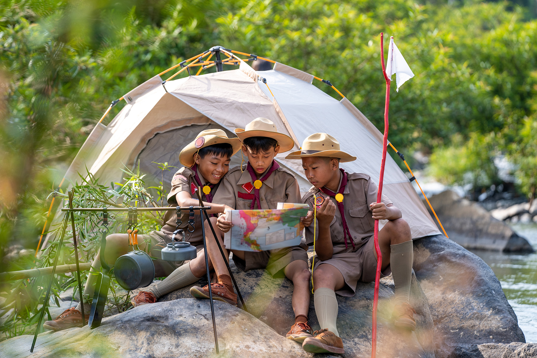 Group of boy scouts in uniform sitting beside a tent and figuring out where to go on the map. They look like they're having fun.
