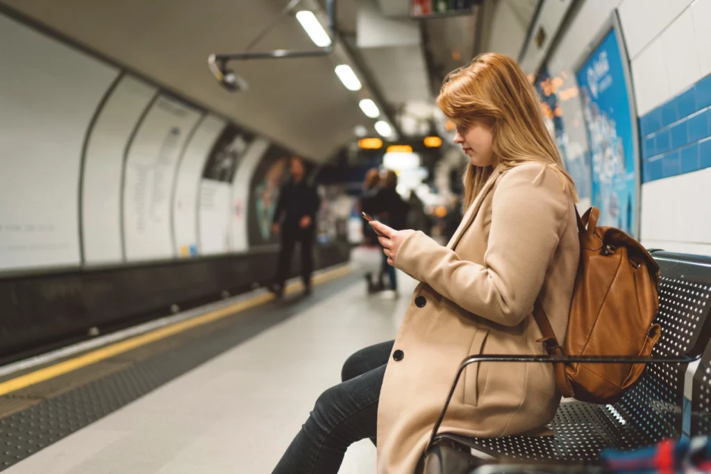 a woman looking down at her phone as she waits for a train to arrive in the London Underground