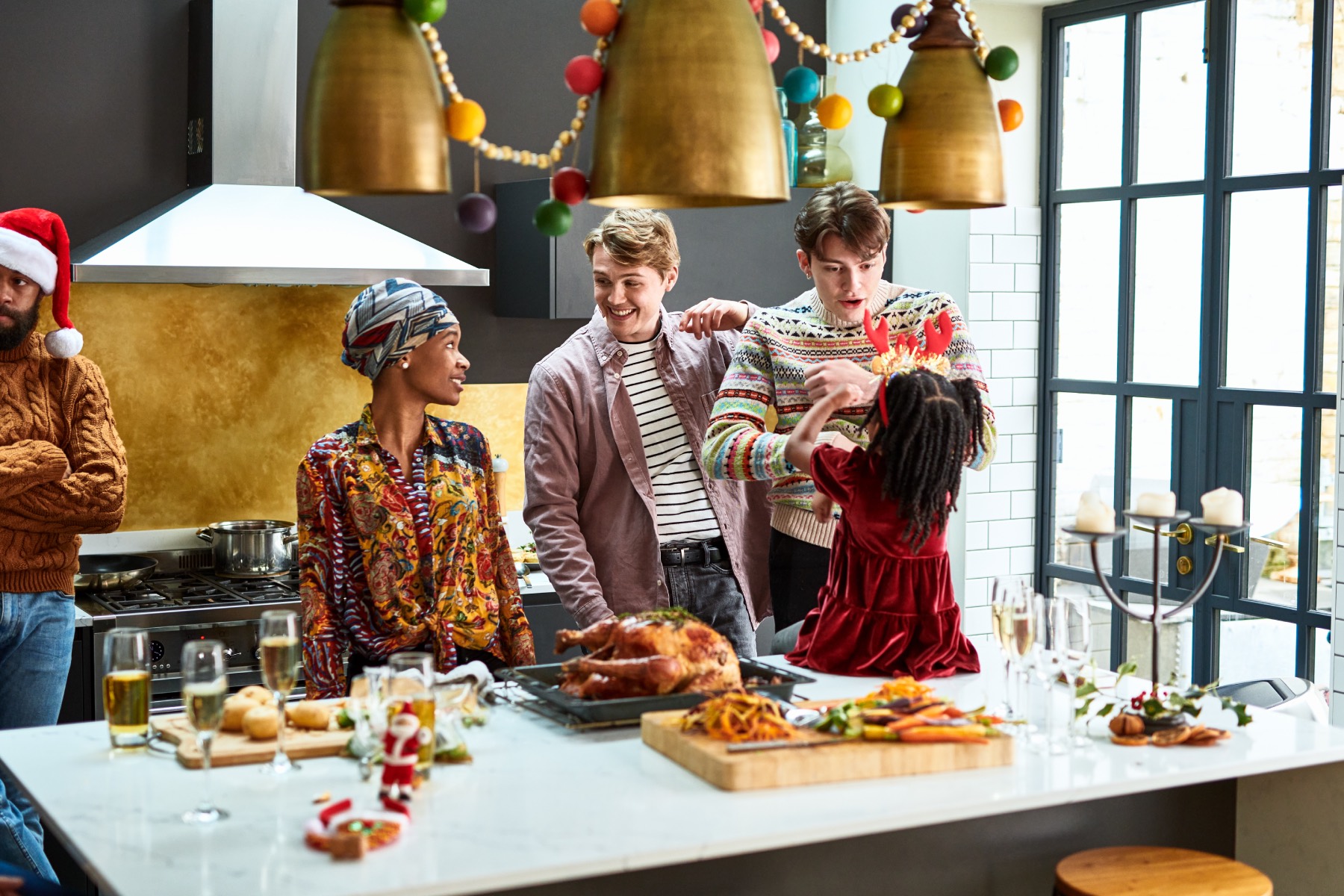 A family stands in a a kitchen chatting, a roast turkey is laid on a table and Christmas decorations hang from the ceiling