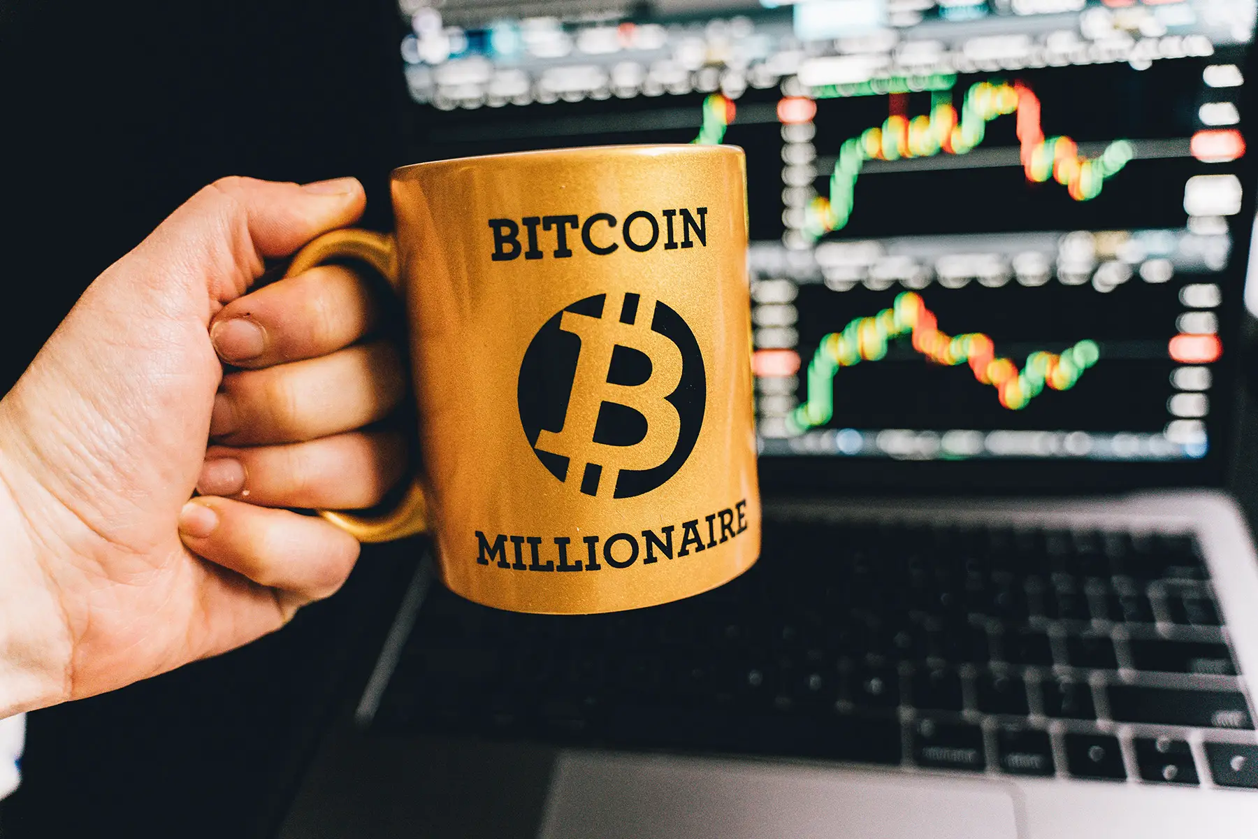 Golden Bitcoin millionaire mug in front of a laptop showing online crypto portfolio