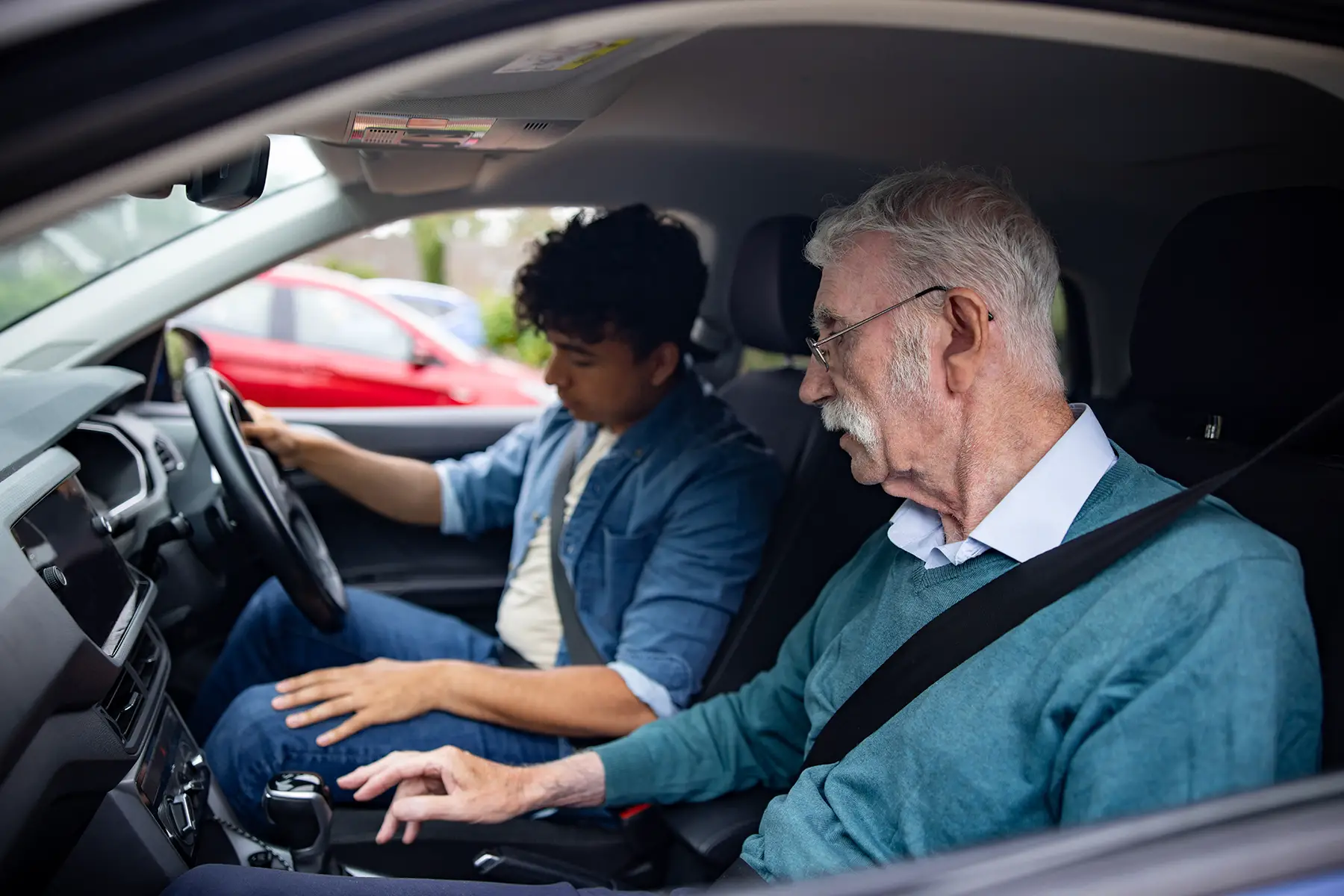 A senior man teaches a younger man to drive.