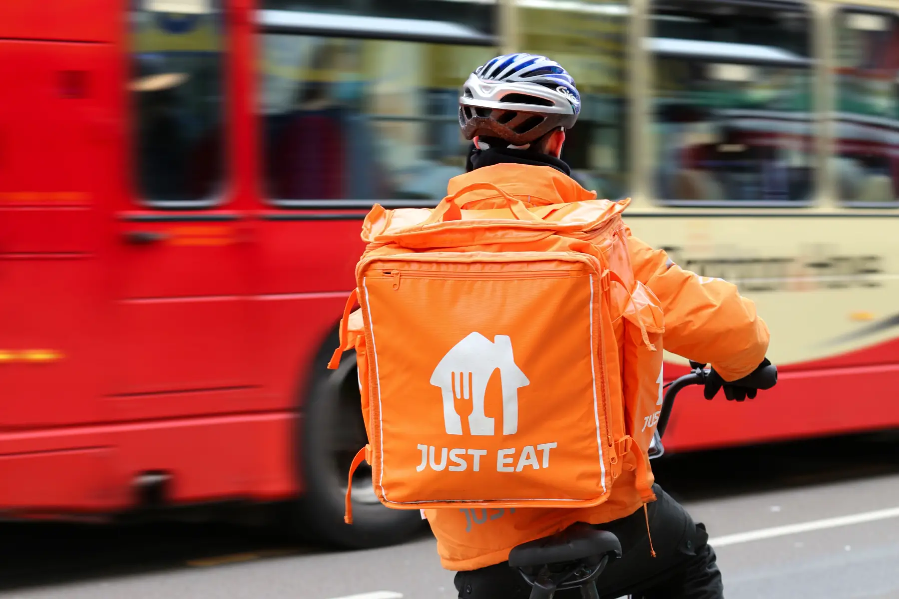 A Just Eat delivery driver on a bicycle, waiting for a bus to pass.