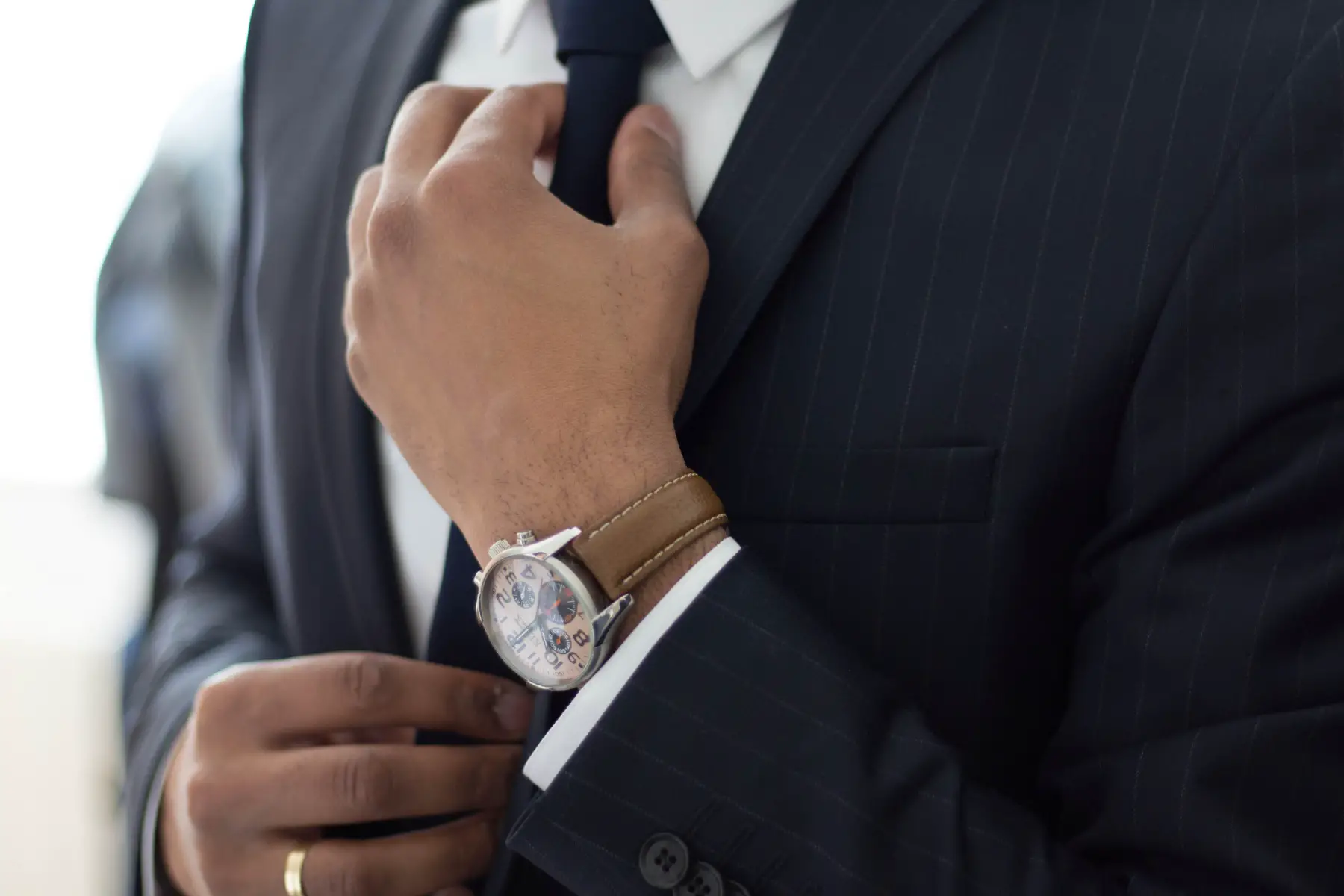 A close-up shot of a man in a smart suit fixing his tie as he gets ready to attend a job interview