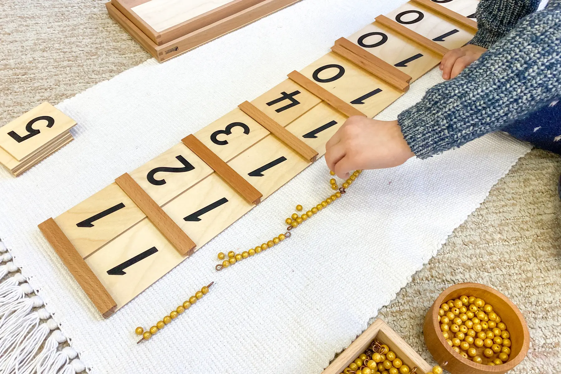 Close up of child's hands working with Montessori wooden numbers and beads, independent primary school in the UK