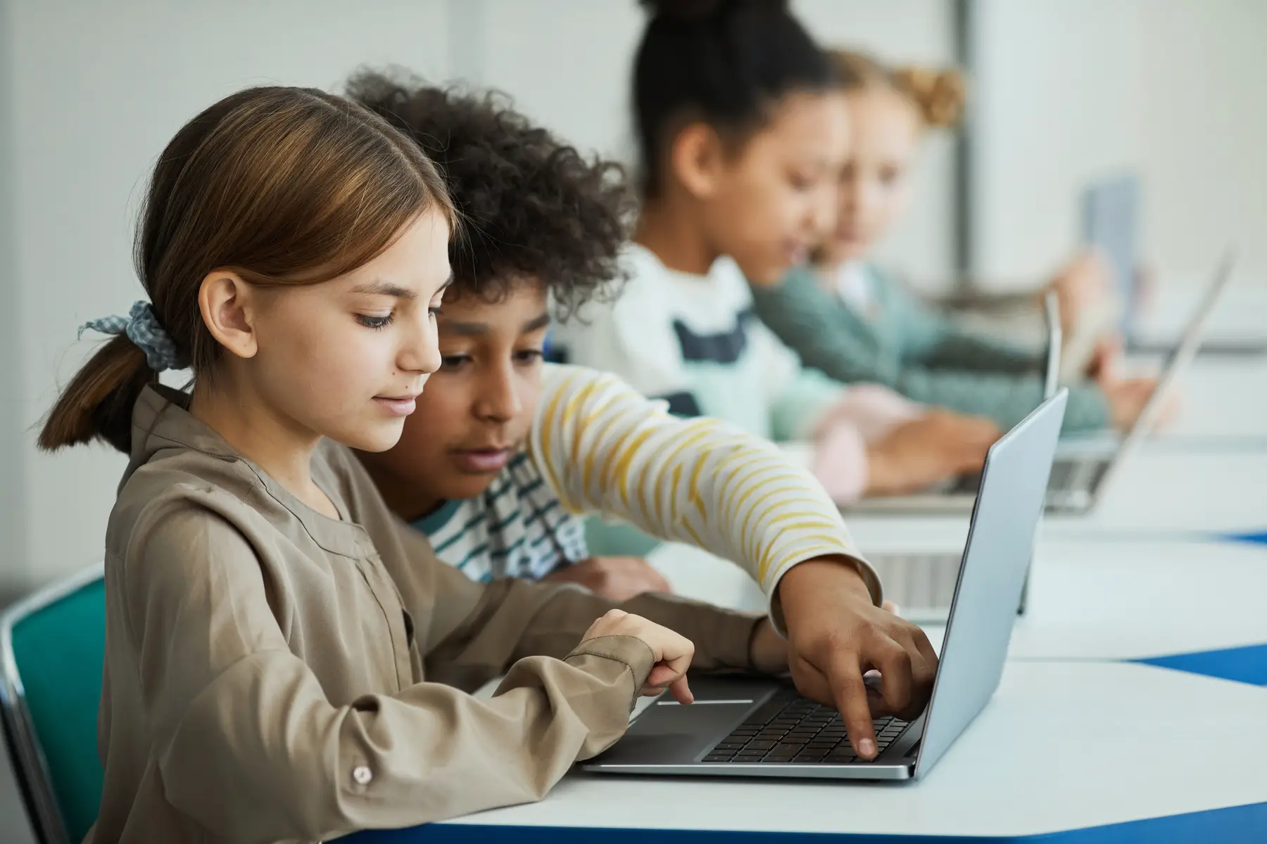Boy helping girl on laptop in a multicultural class