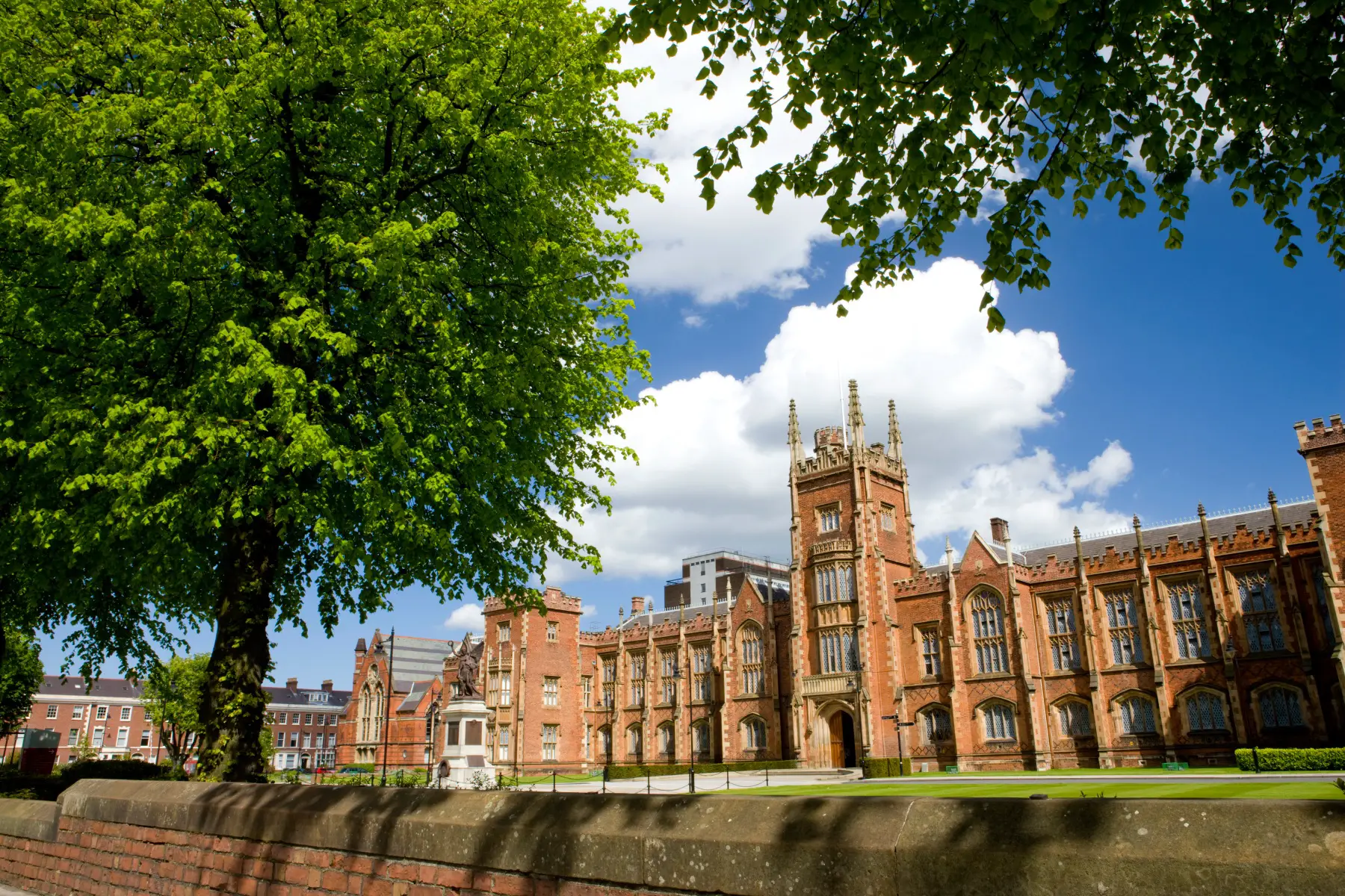 Queen's University Belfast, a gothic-style brown building on a sunny day, with trees in the foreground