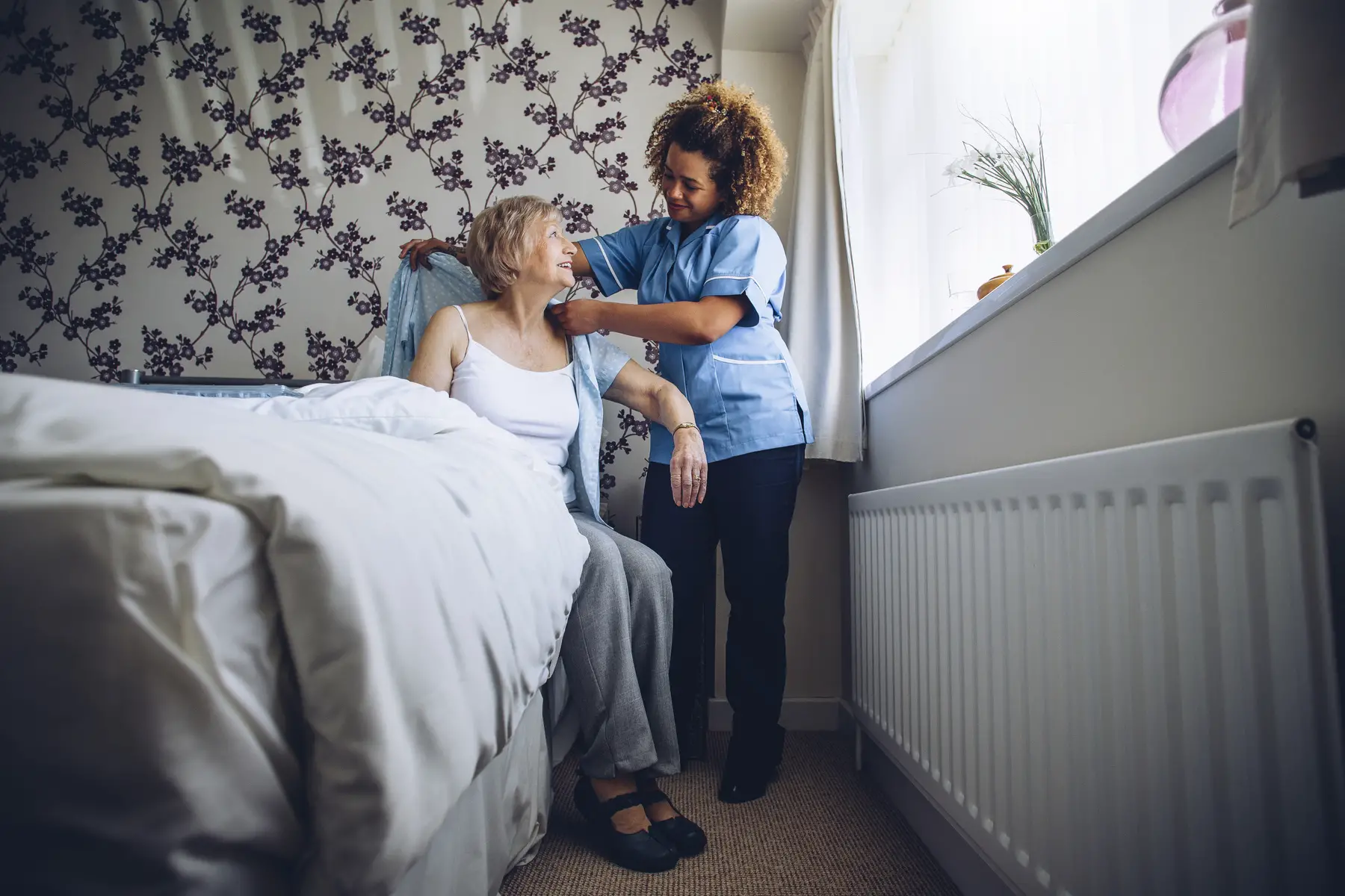 Care at home provider helping a senior woman get dressed in her bedroom