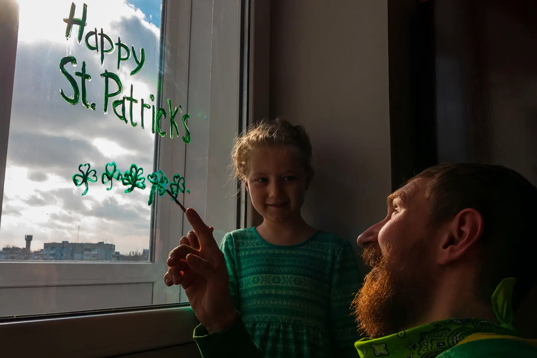 Daughter at home with dad painting window for St. Patricks Day, a public holiday in Northern Ireland