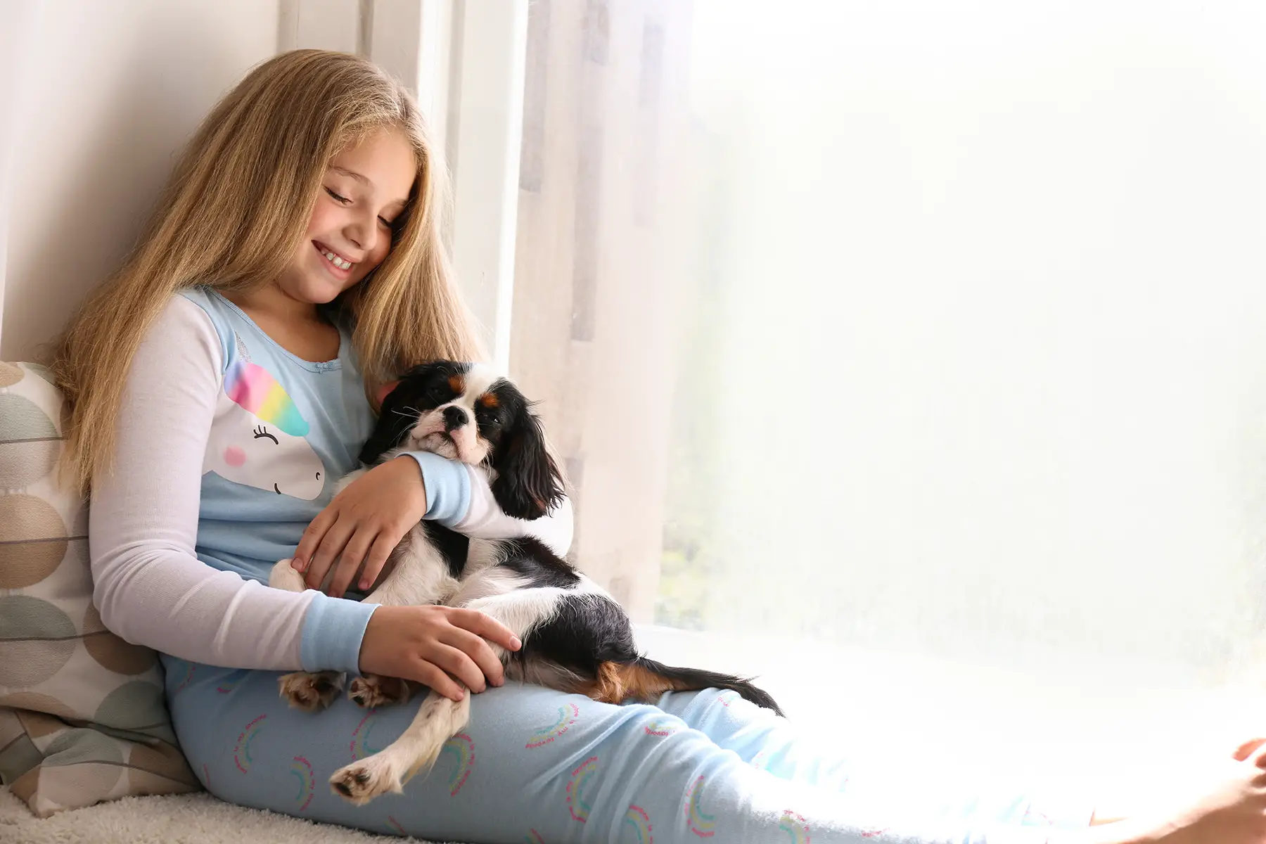 a little girl cuddling her Cavalier King Charles Spaniel puppy at home