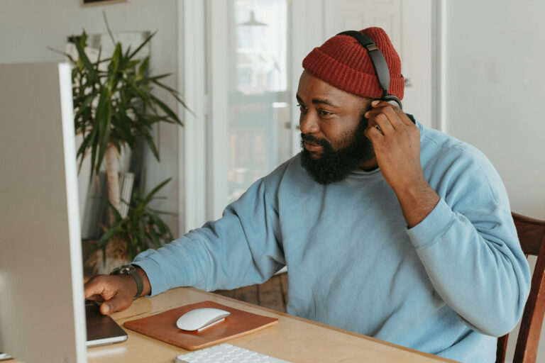 Man adjusting his headphones while sitting at his home office desk.