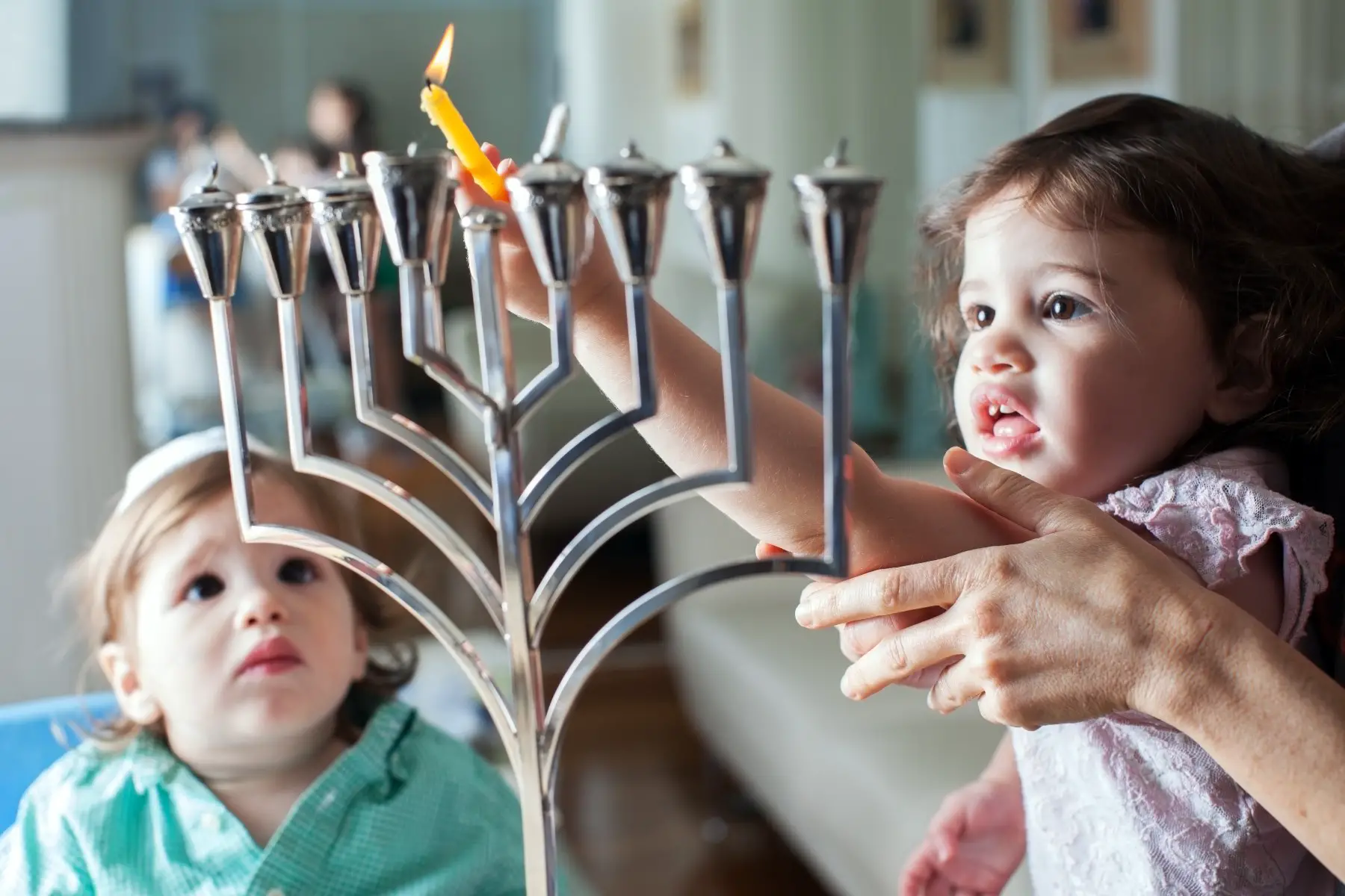 A young girl lights the Hanukkah menorah with help from an adult.