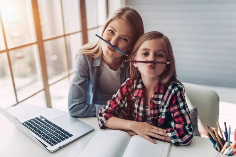 Mom and child sitting at a laptop and book balancing pencils on their lips
