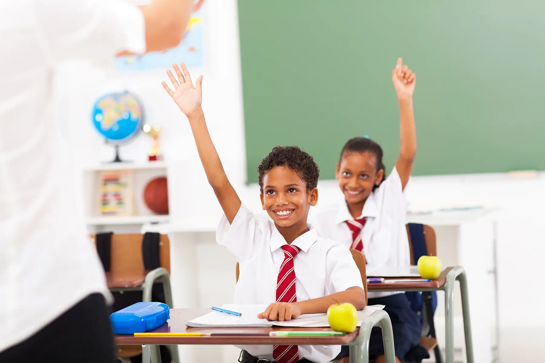 Children in uniform raising their hands for the teacher