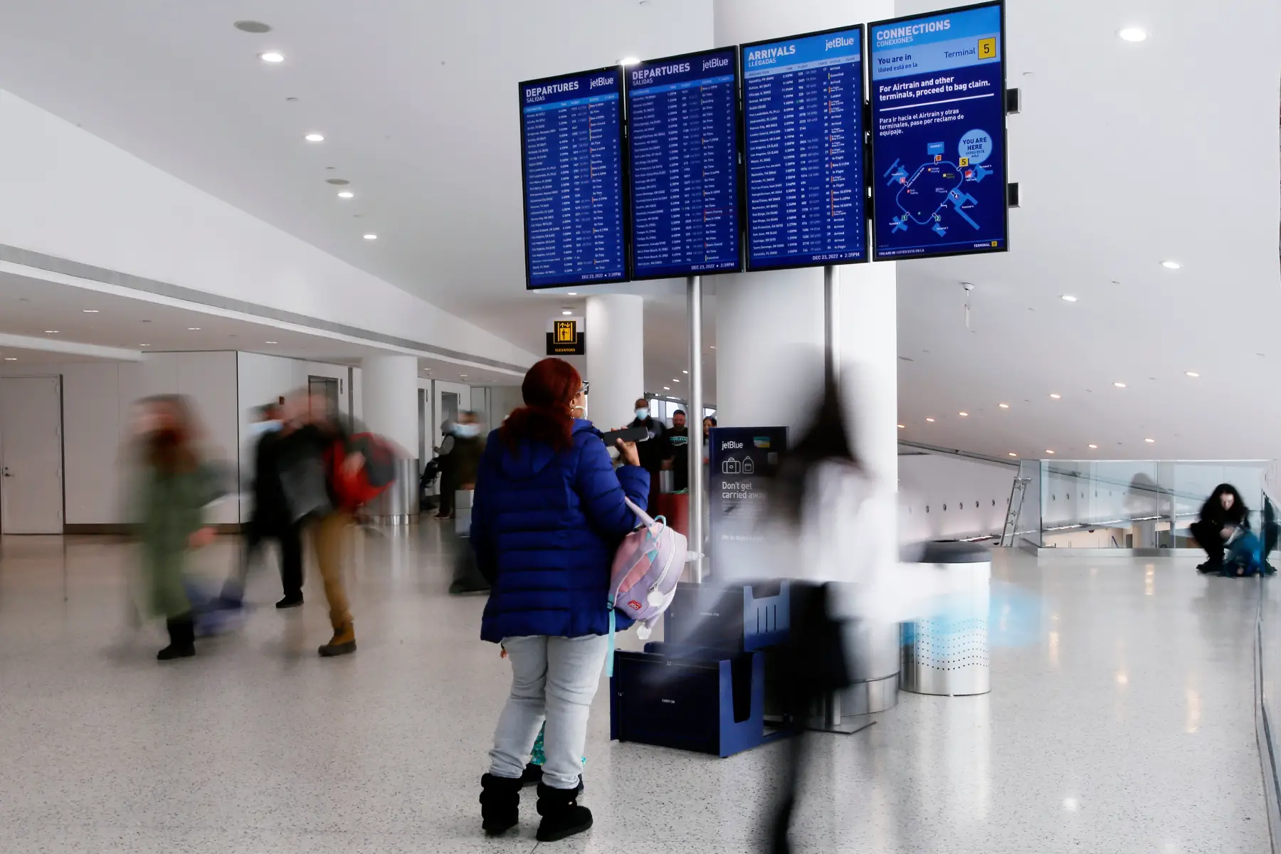 Woman checking departure board amid people rushing at JFK airport