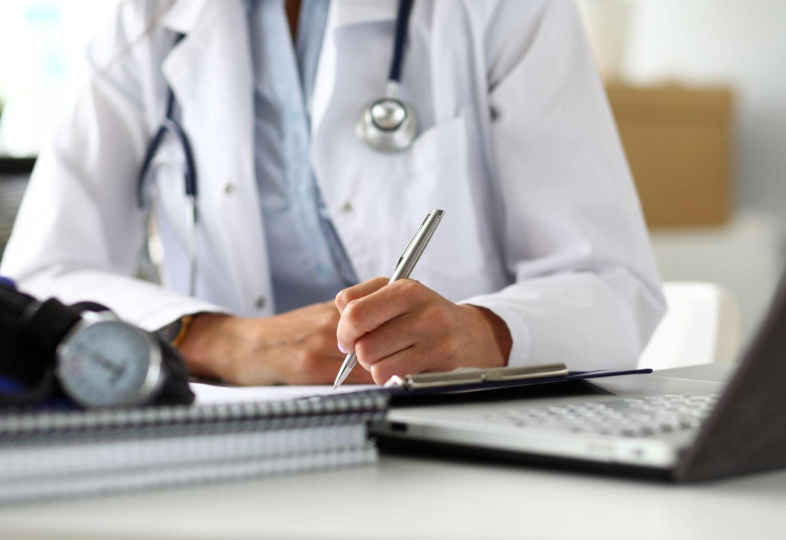 A doctor writing notes at a desk with a laptop, representing health insurance options for Australians living abroad.