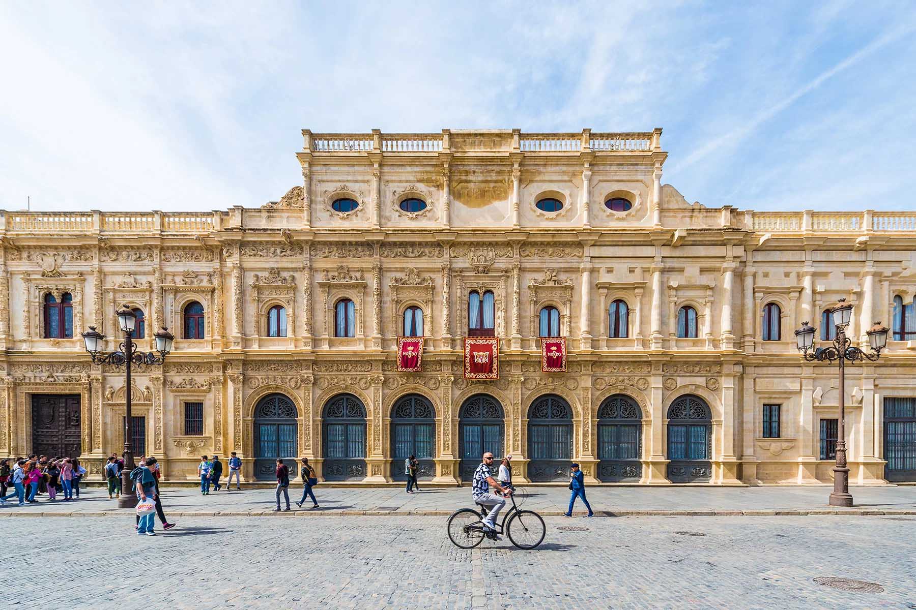 People cycling and walking by the Casa consistorial de Sevilla, Spain