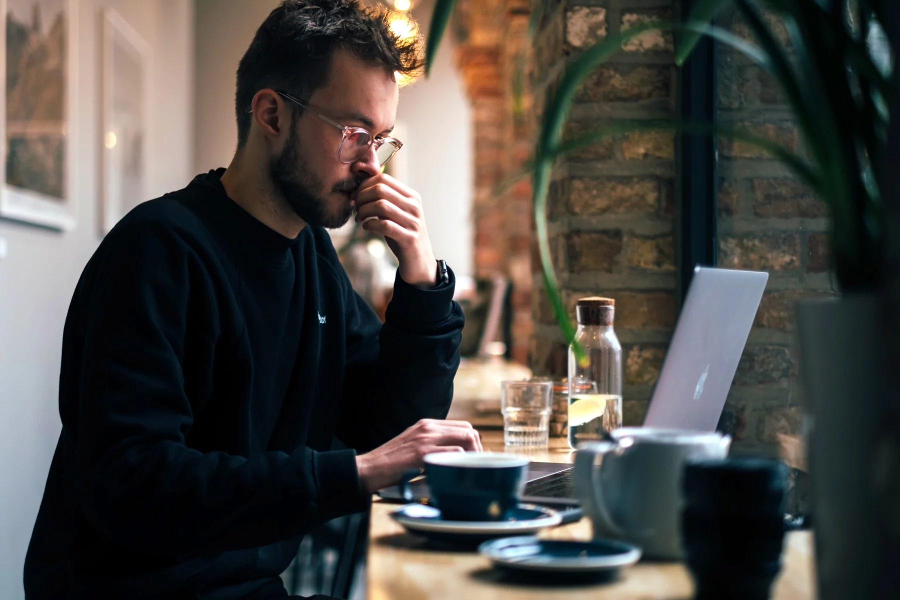 A man with glasses sits at a desk in front of his laptop.