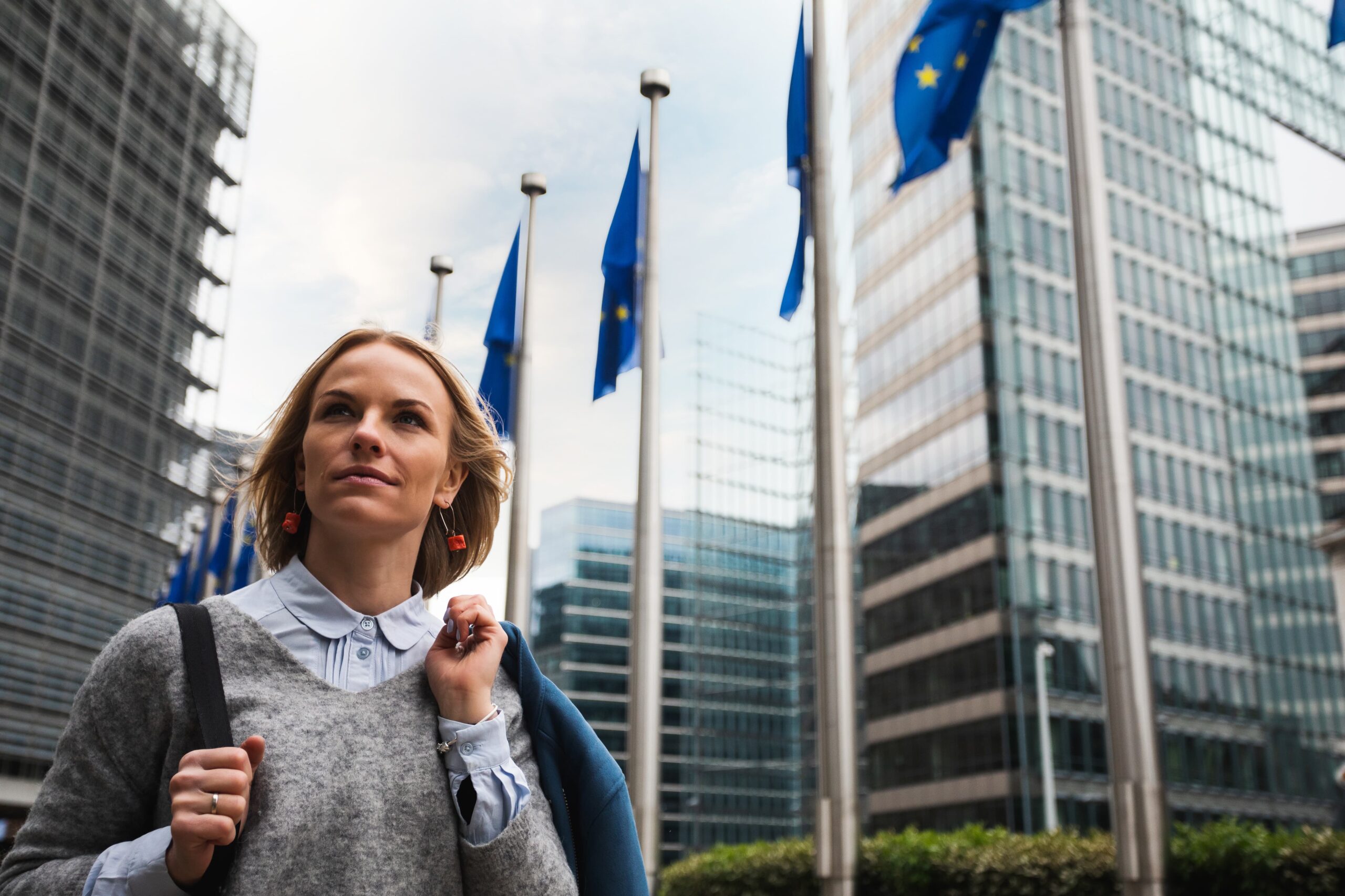 Woman walking in front of the European Union offices in Brussels with EU Flags flying in the background.