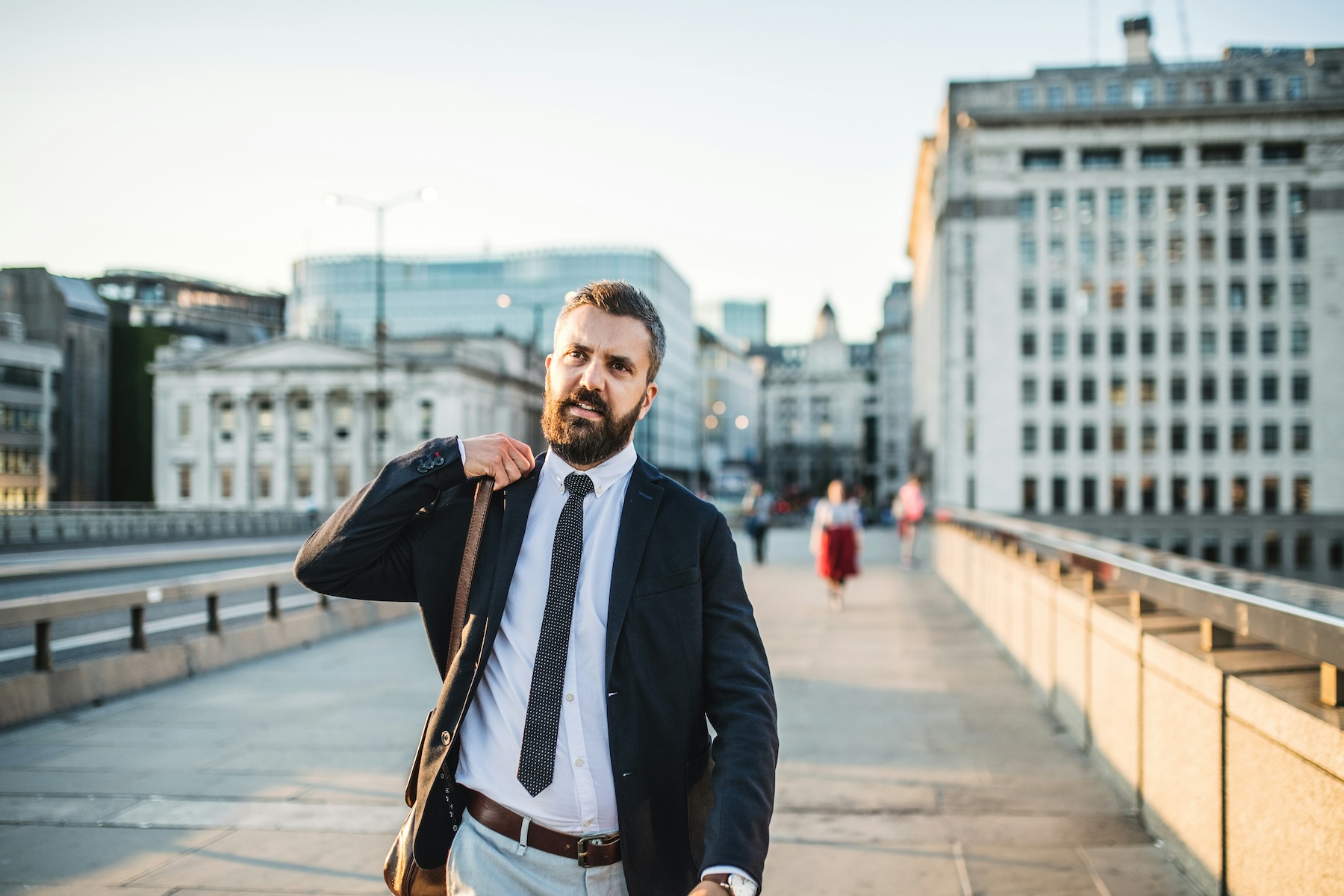 A business man dressed in a suit commutes on foot across a bridge