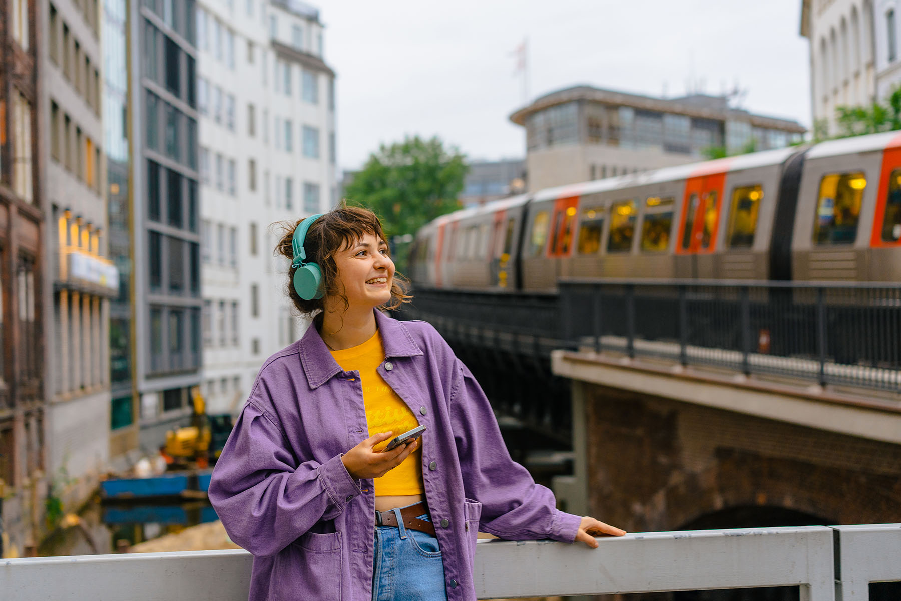 Woman listening to music on her headphones with the subway of Hamburg in the background.
