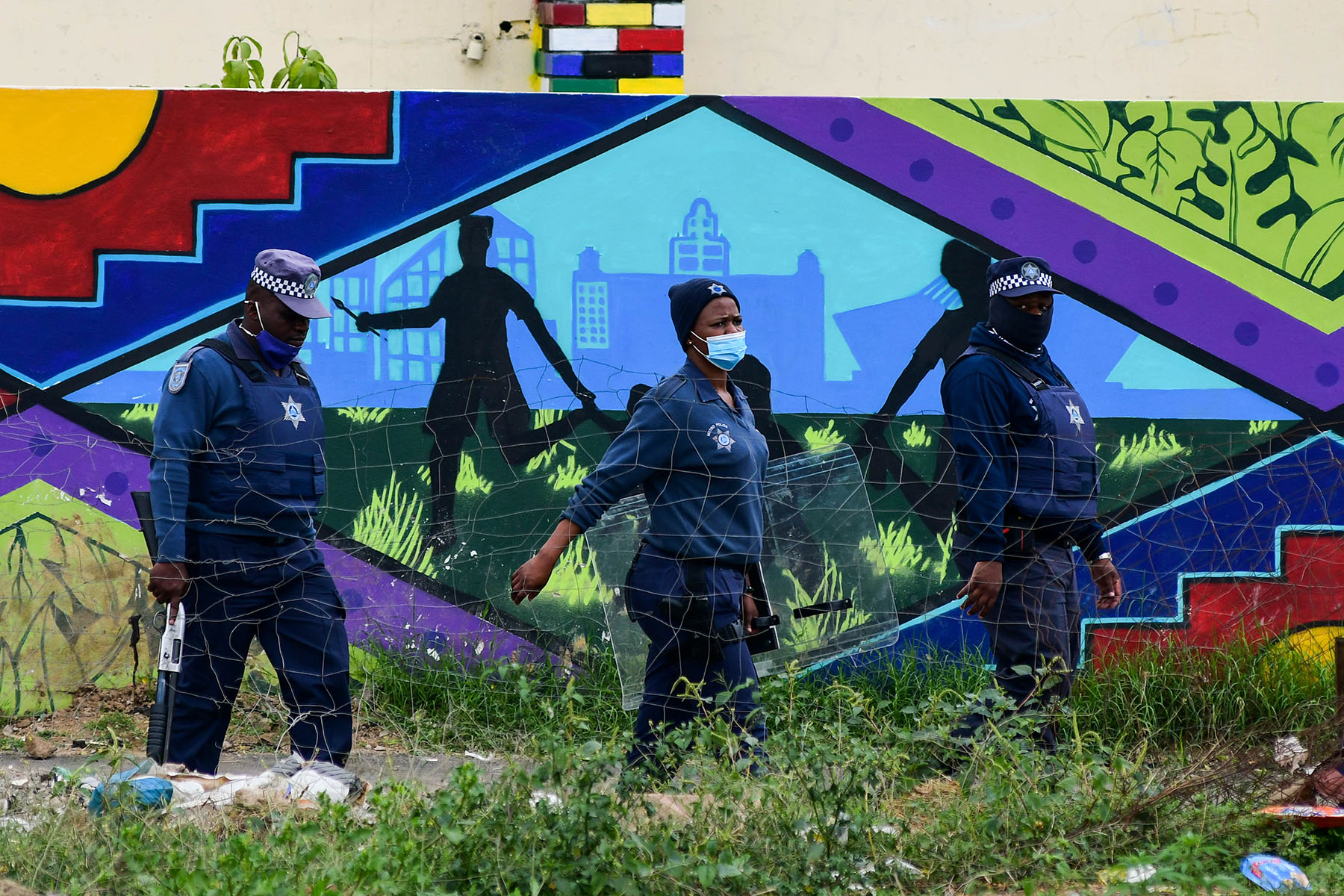 South African police officers walk past a mural on a wall while investigating a crime