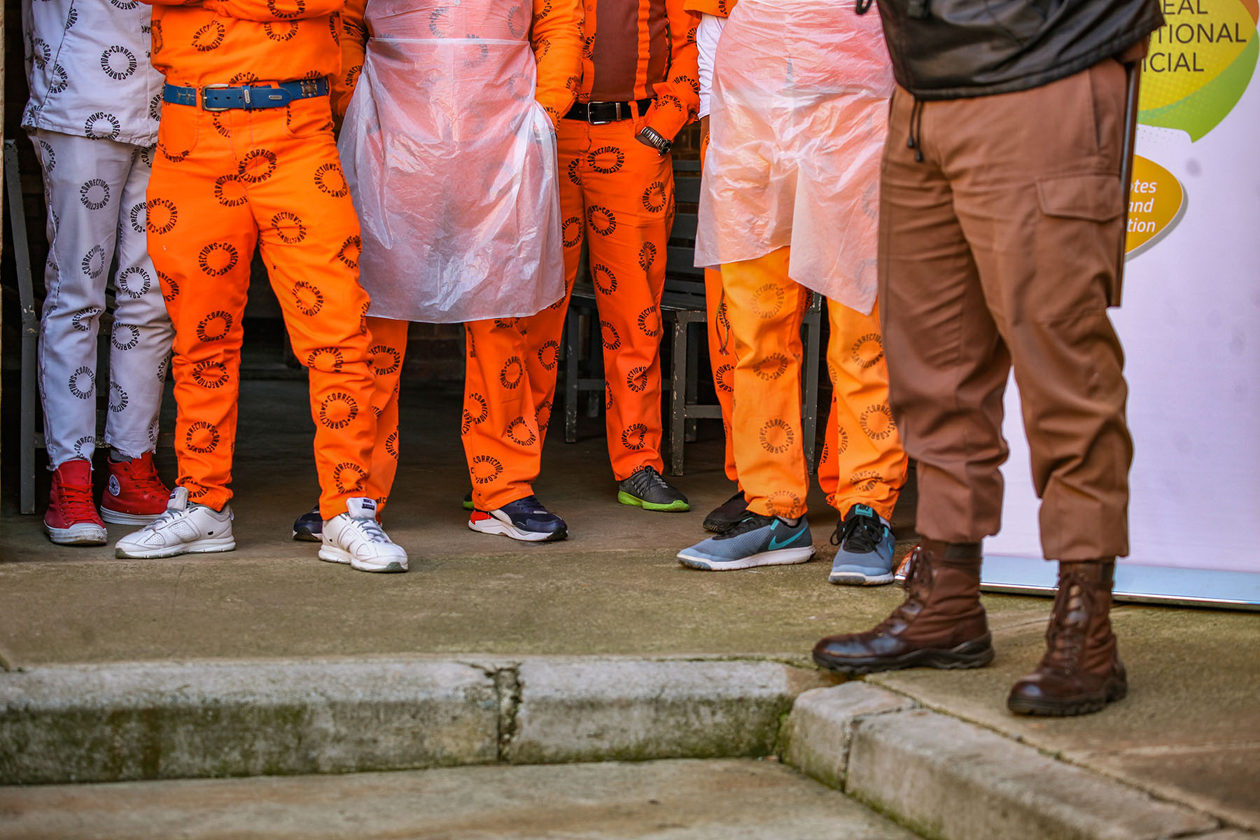 Legs of prisoners (orange uniforms) and a guard (brown uniform)