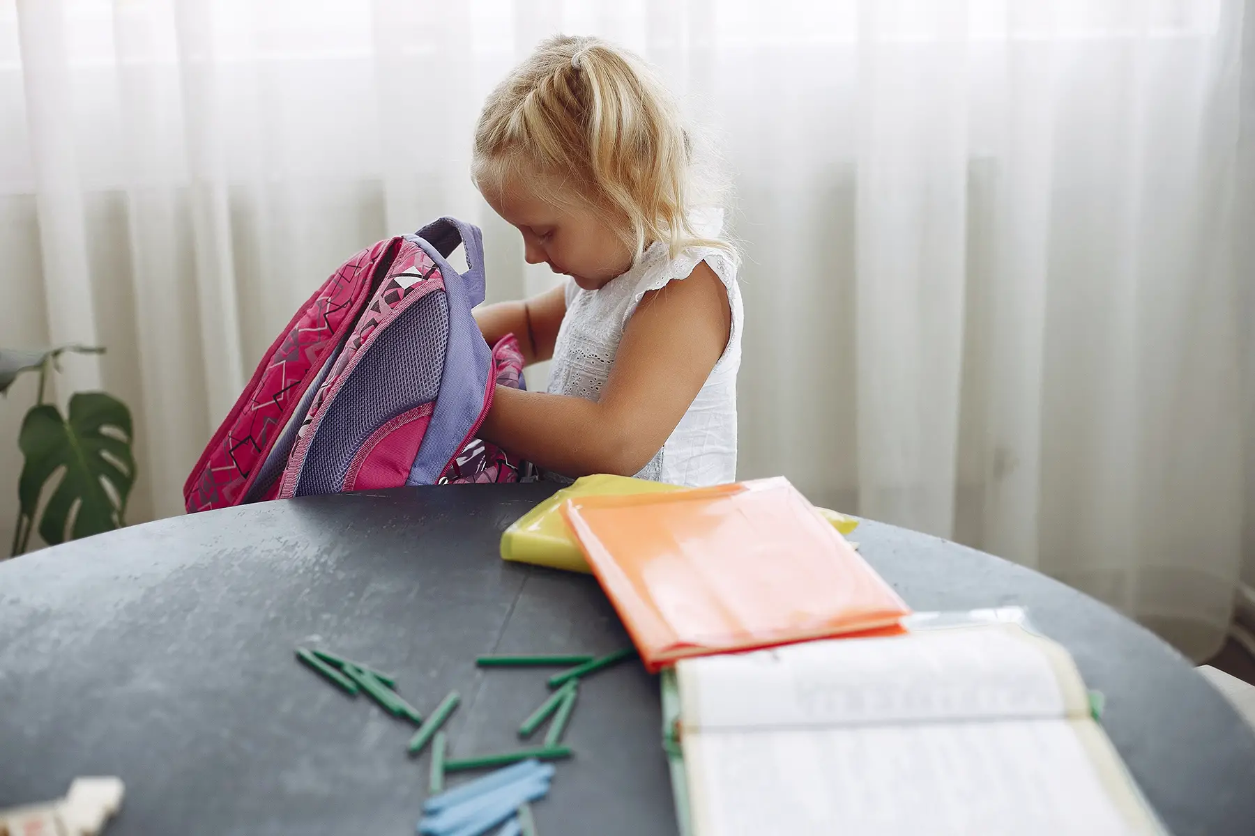 Pre-schooler (little blond girl) looking at new school bag, application forms next to her on the table