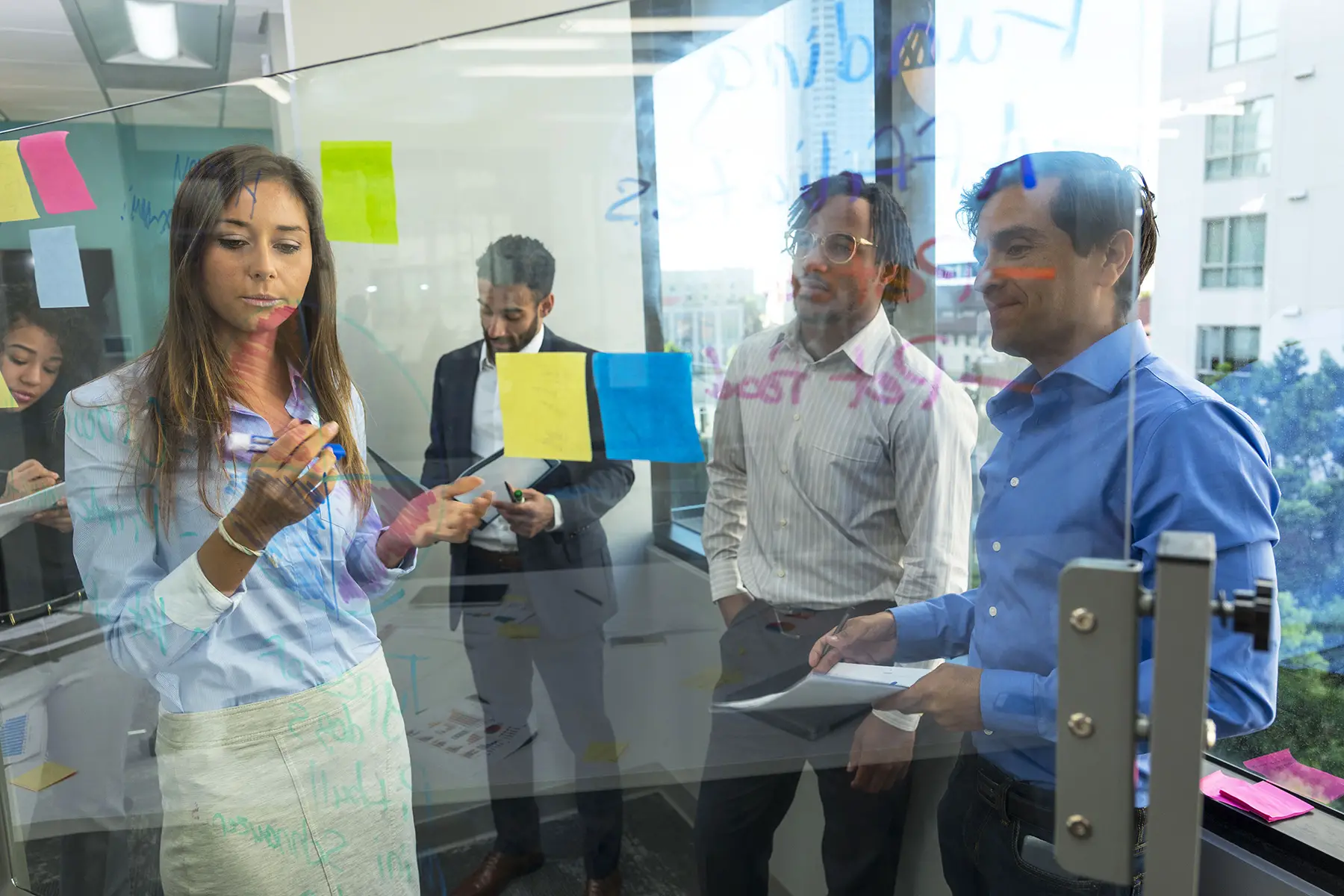 Business meeting - three men and a woman standing in office looking at writing on a window, due to the gender pay gap in South Africa, women often get lower wages than men for doing the same job