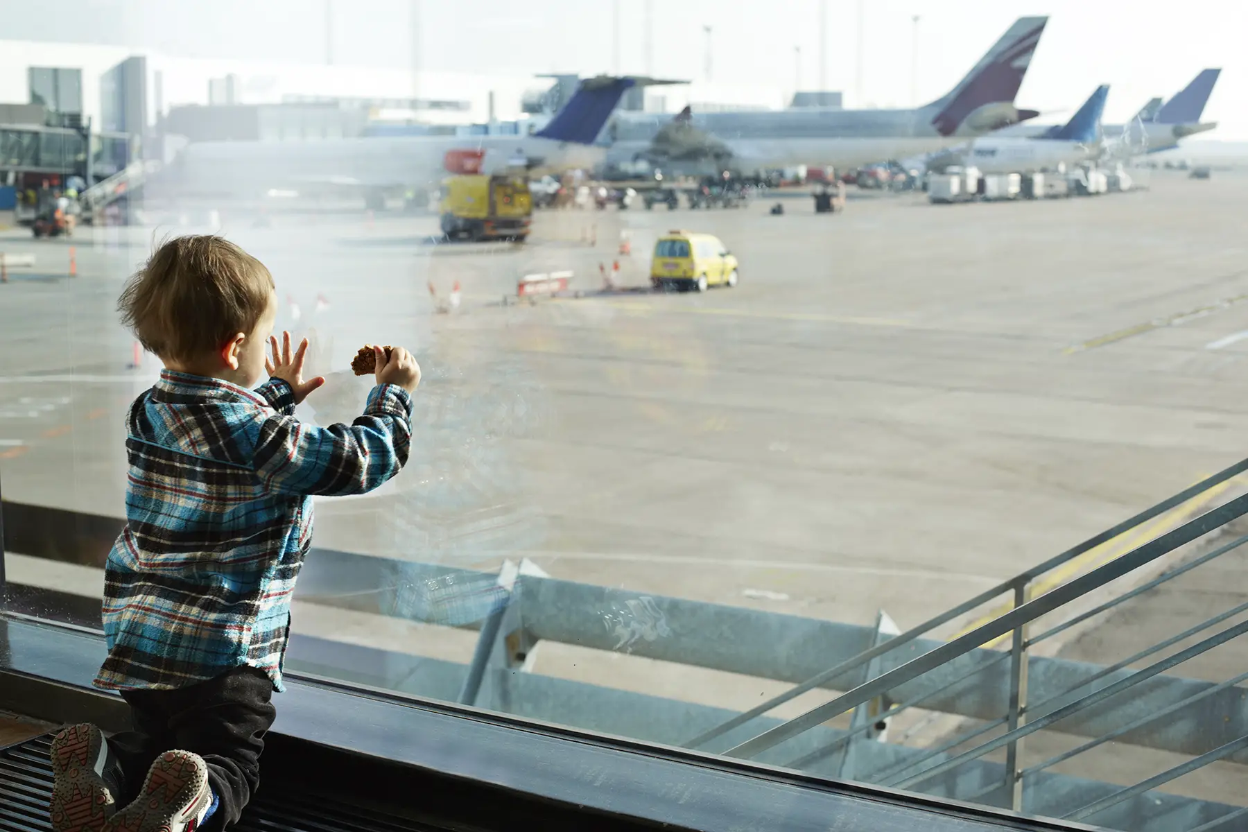 Toddler standing on knees looking through big window at planes at Cape Town airport in South Africa, his family would need visas to be move there