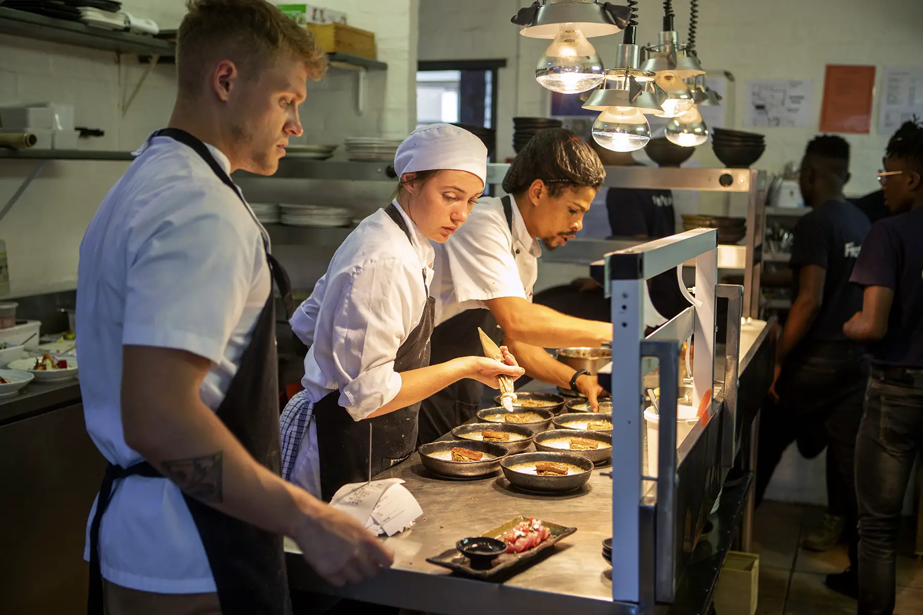 Three chefs preparing food in a restaurant kitchen at Hemel-en-Aarde winery and restaurant