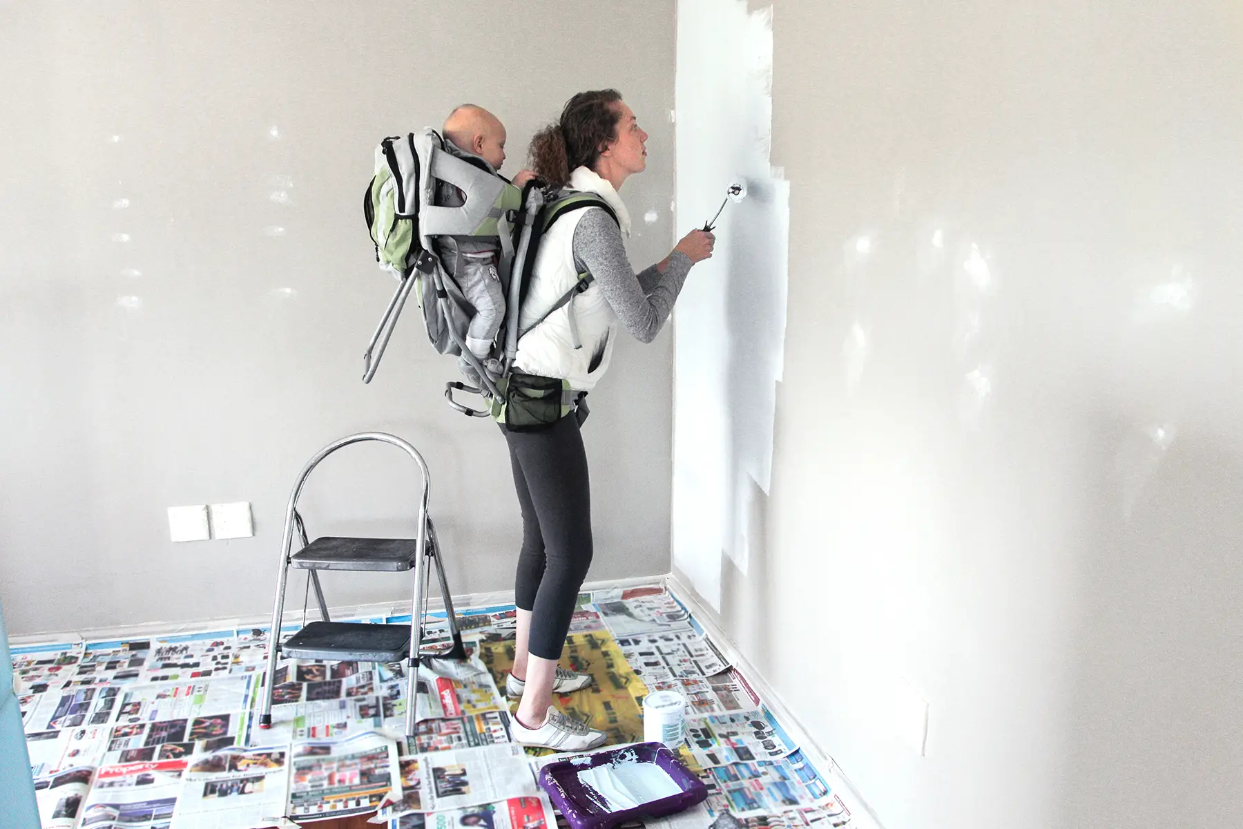 A mum carrying baby on her back paints the wall of a room, home improvements
