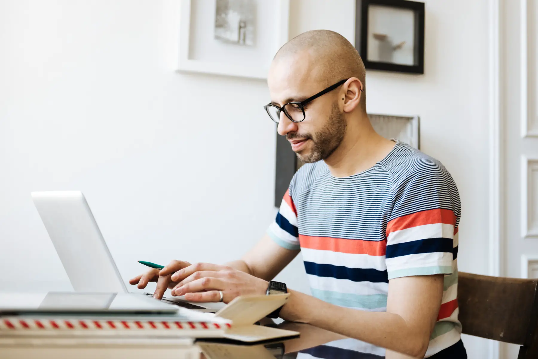 a bald man sitting at a desk at home and working on his laptop