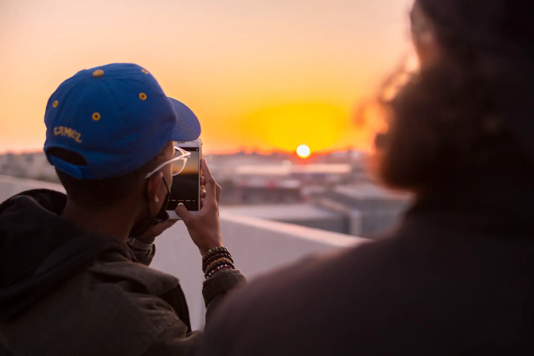 Man using his cell phone to take a picture of the sun set.