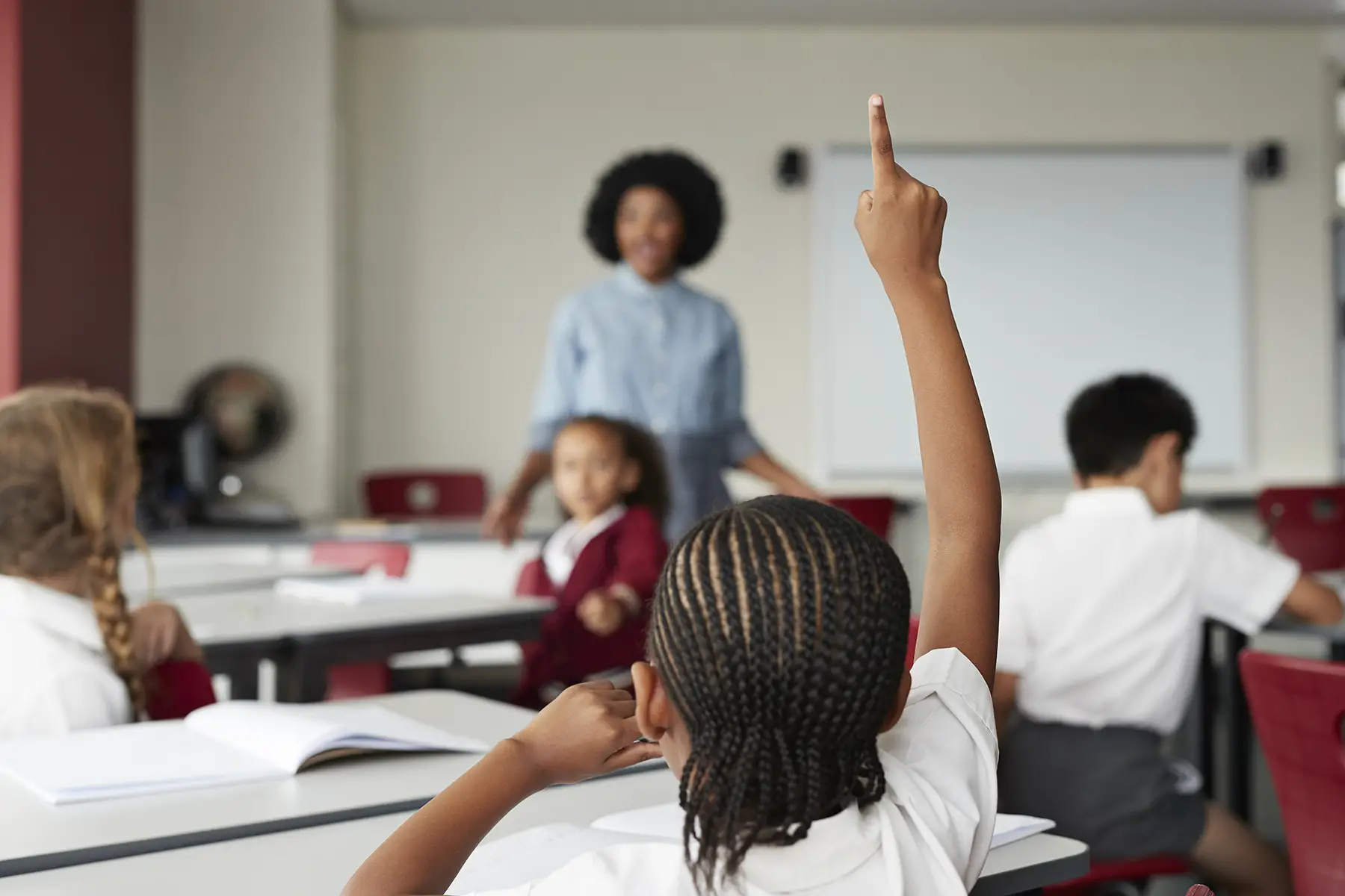 Child raises hand to answer question in primary school classroom