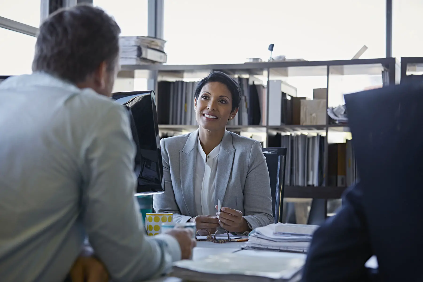 Confident smiling businesswoman discussing with coworkers at desk in an office.