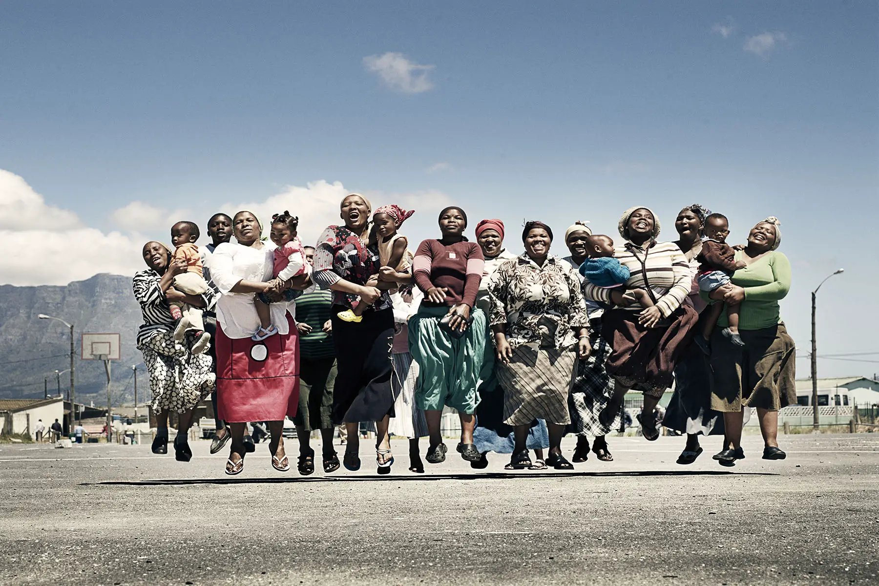 Group of women and children jumping and laughing, outside, mountain in background, Western Cape