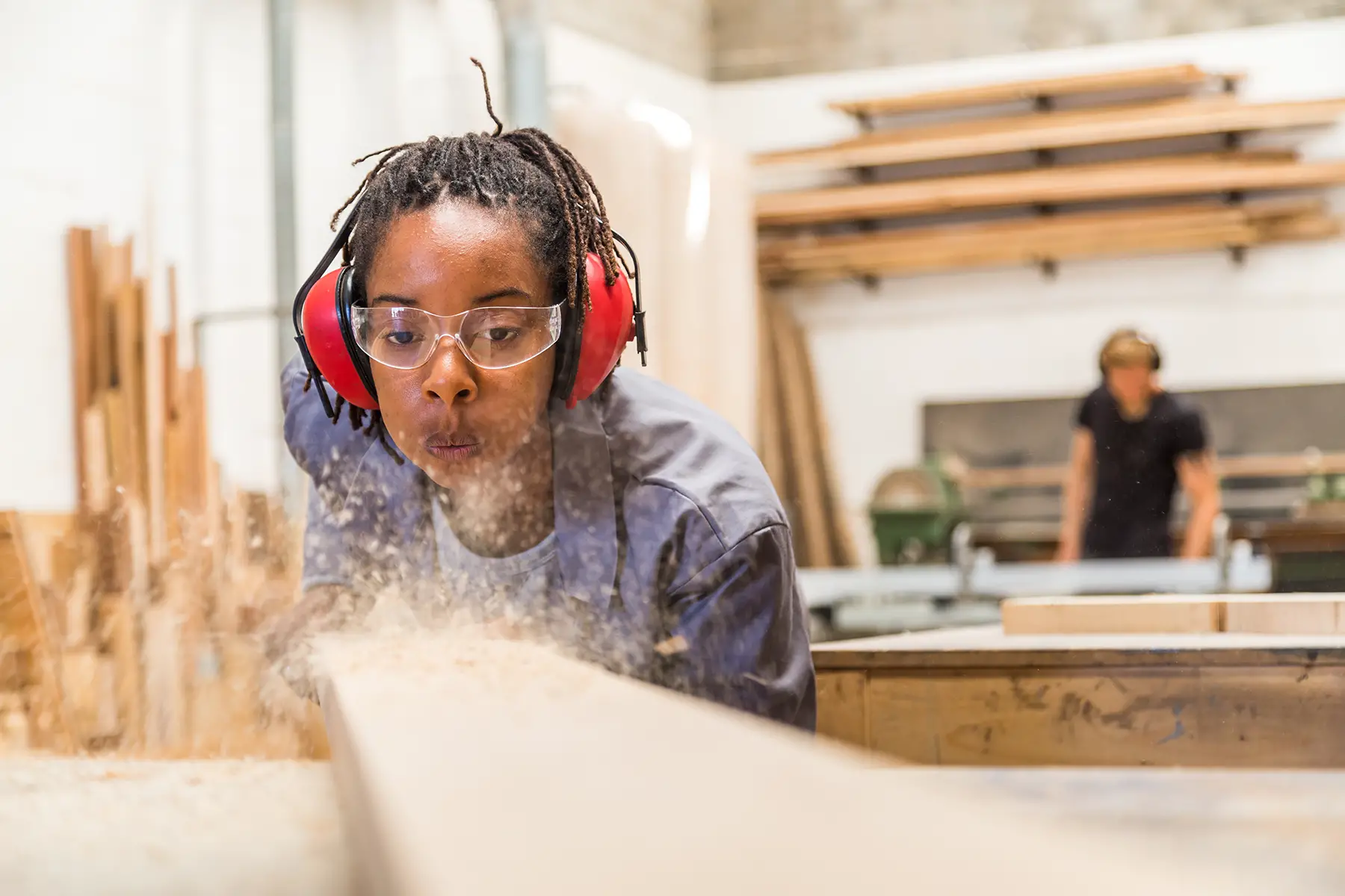 Secondary student in trade school doing carpentry, blowing wood dust