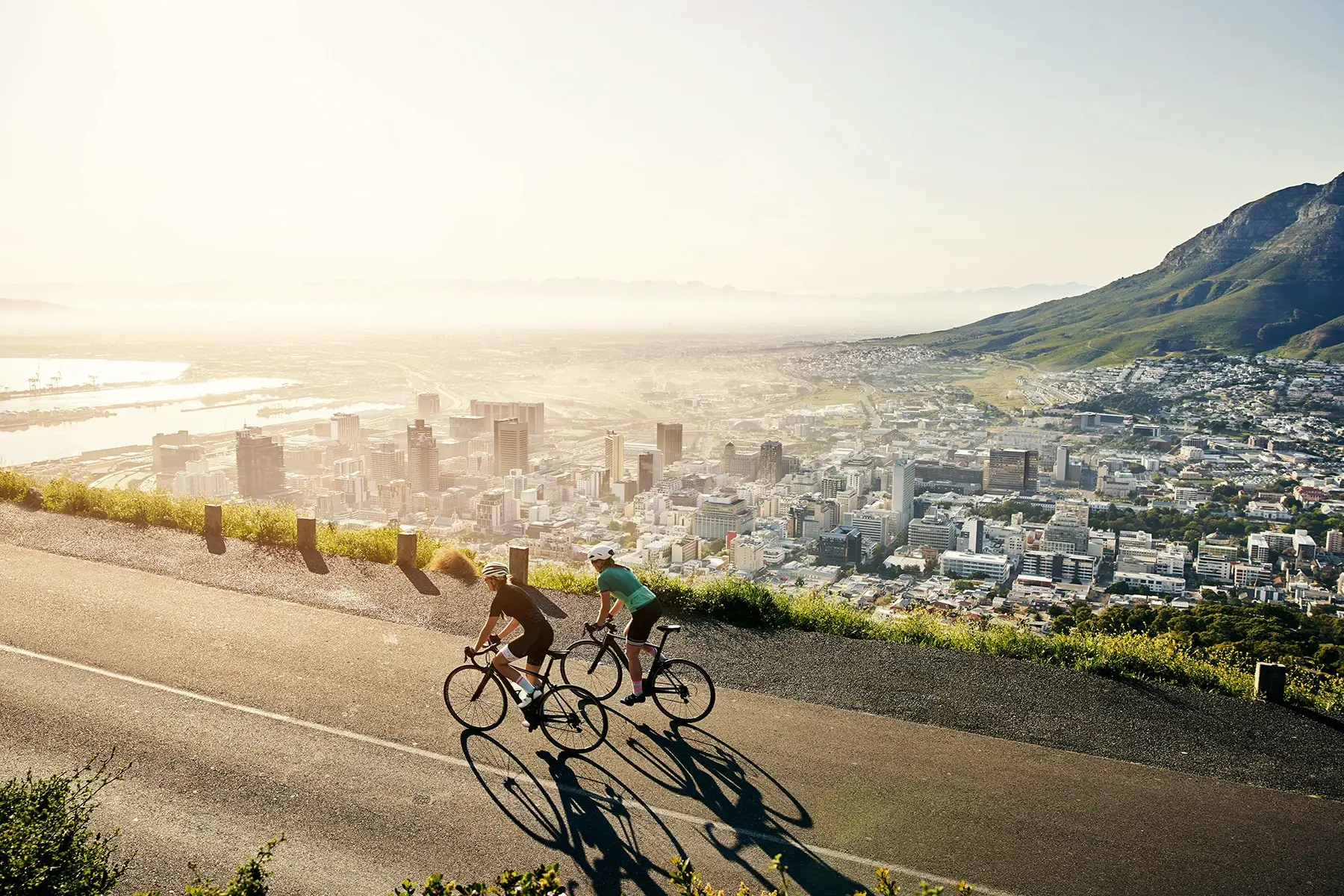Two cyclists on a quiet road early morning ride with the Cape Town skyline below