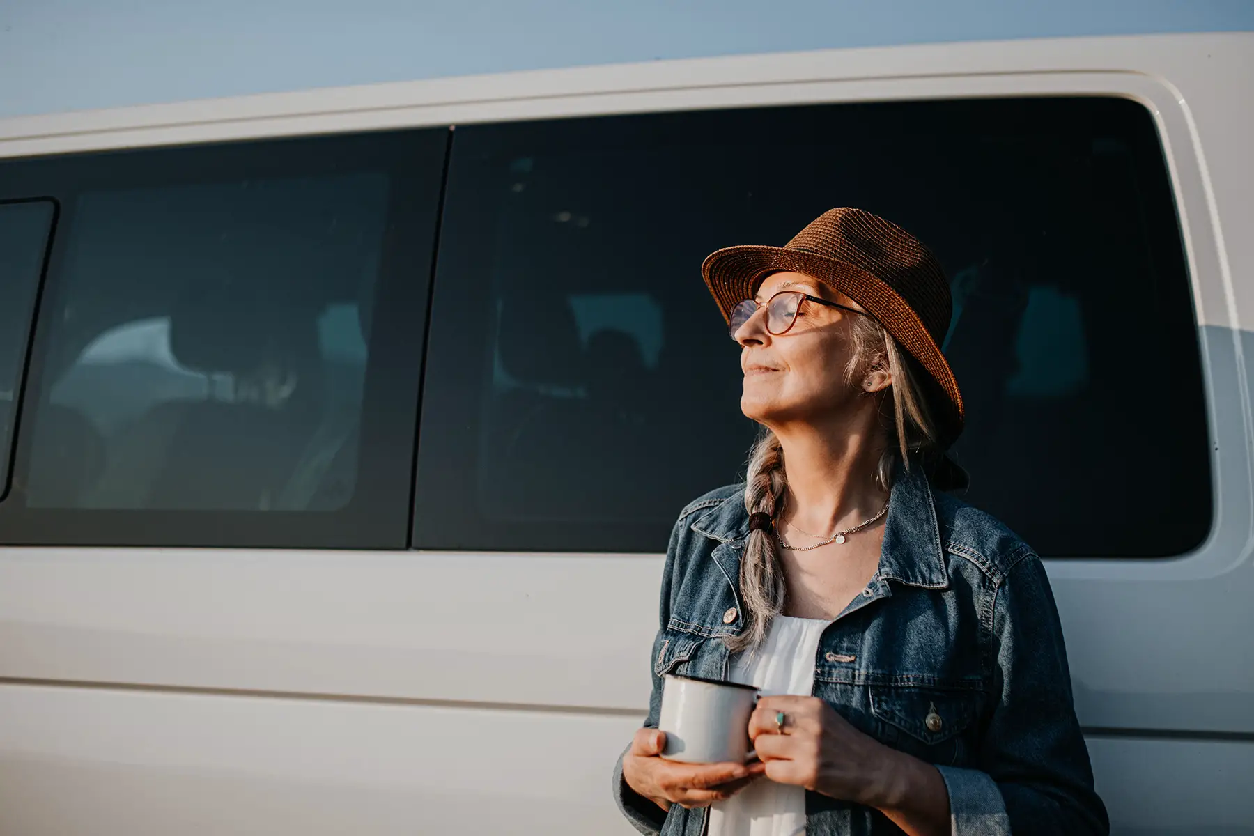 Woman with menopause leaning against van and enjoying a cup of coffee in the sun