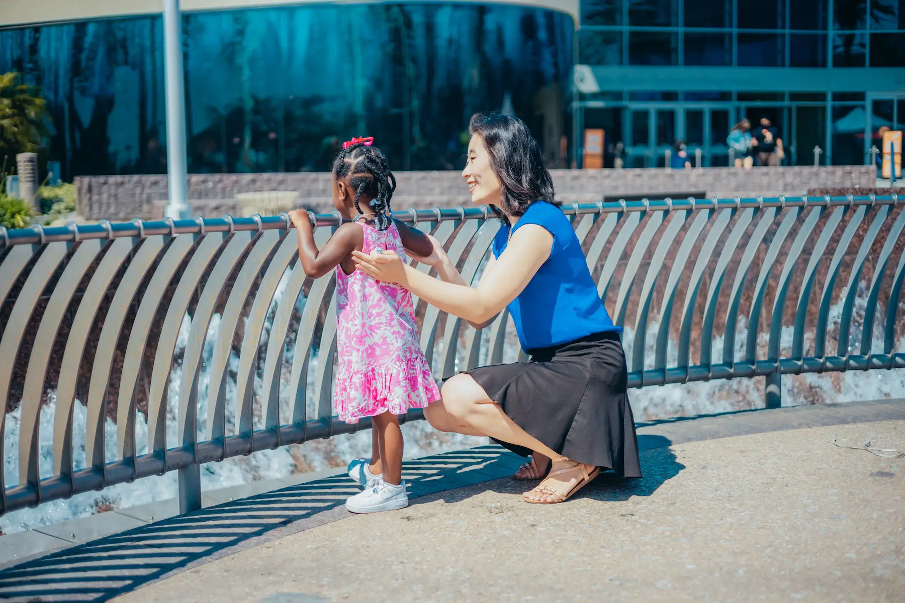 Young girl stands watching a water fountain with her adoptive mother holding her arms